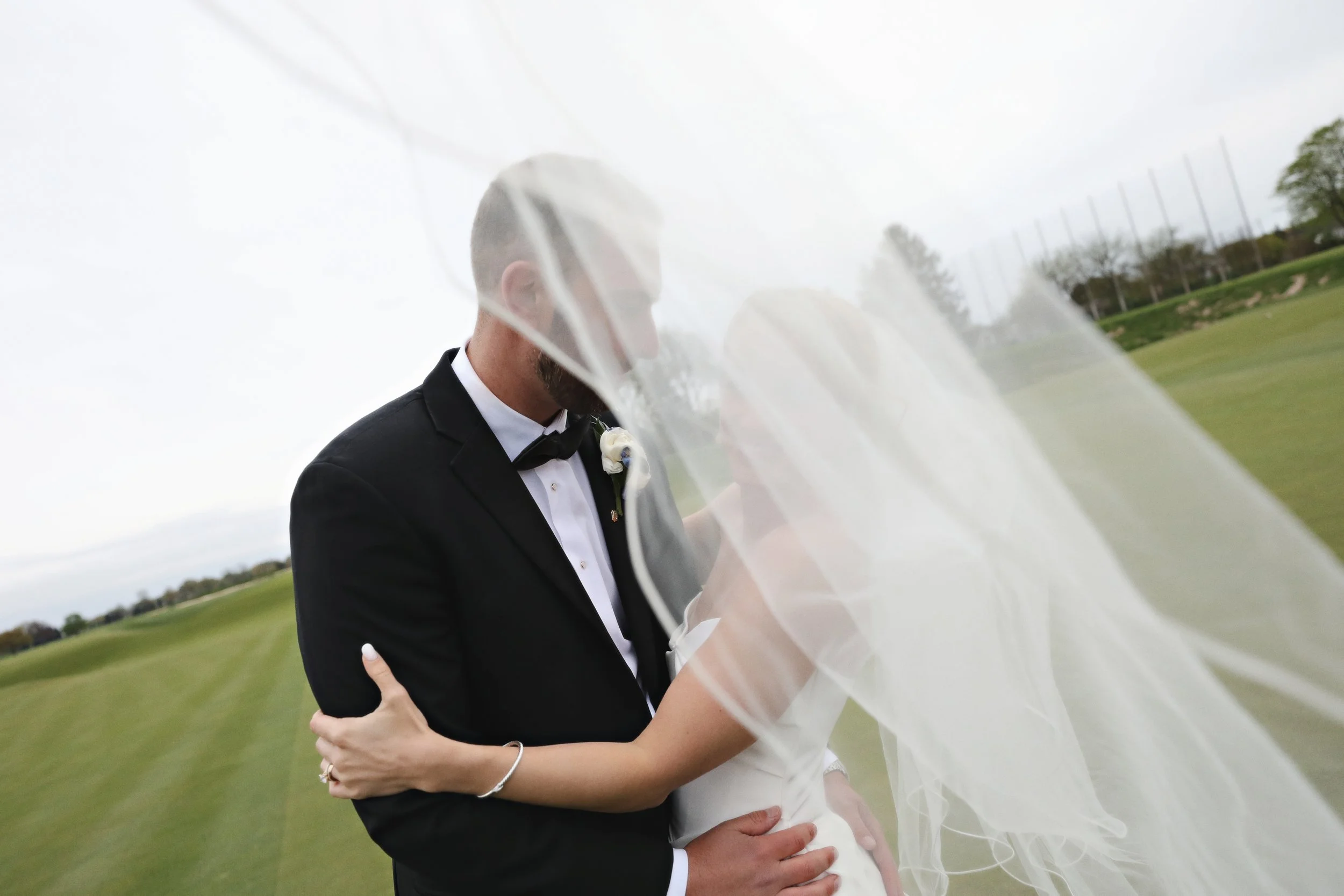 A bride and groom sharing a kiss on a golf course, with the bride's veil partially covering their faces.