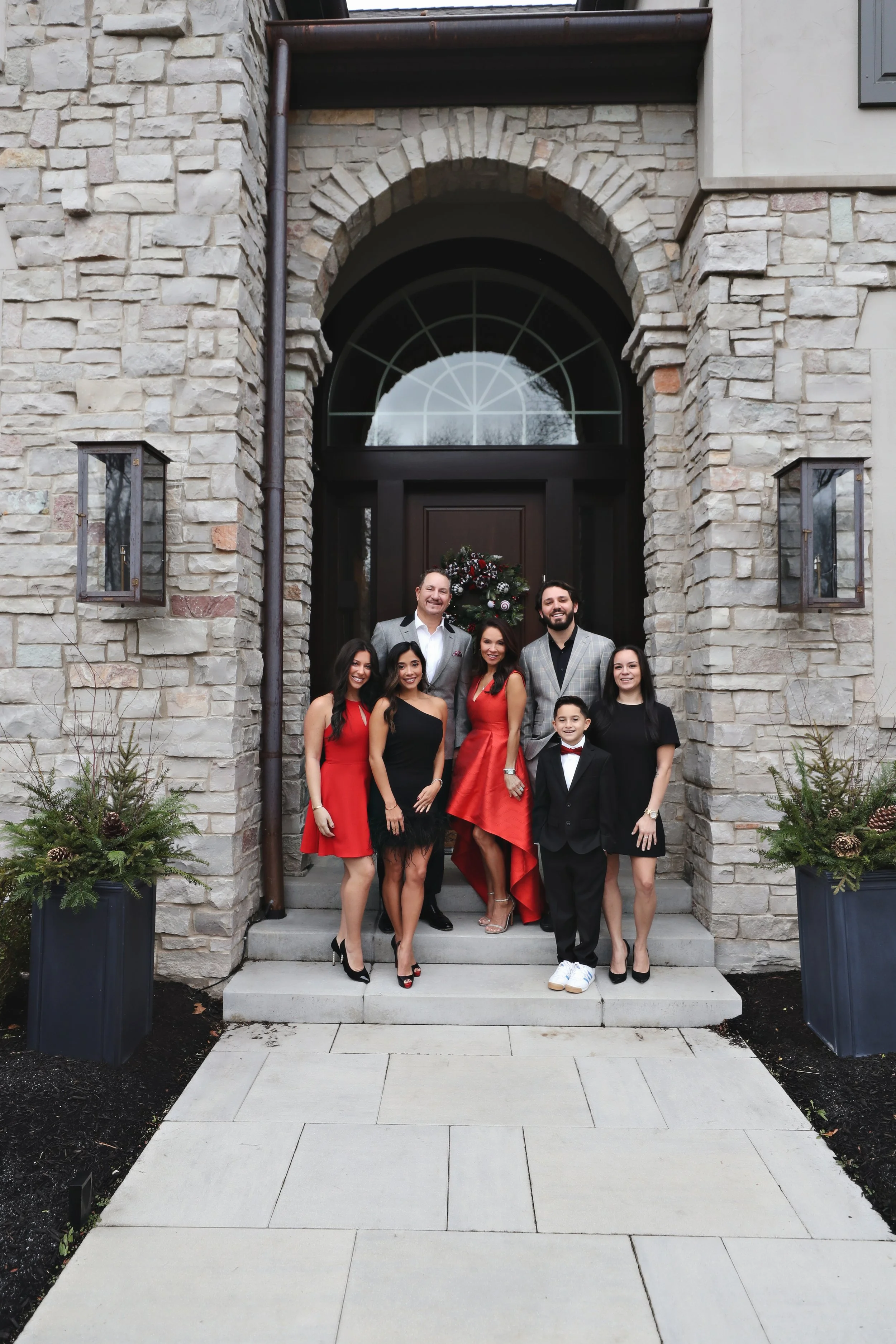 Group of seven people standing on steps outside a stone house decorated with a Christmas wreath and greenery on either side