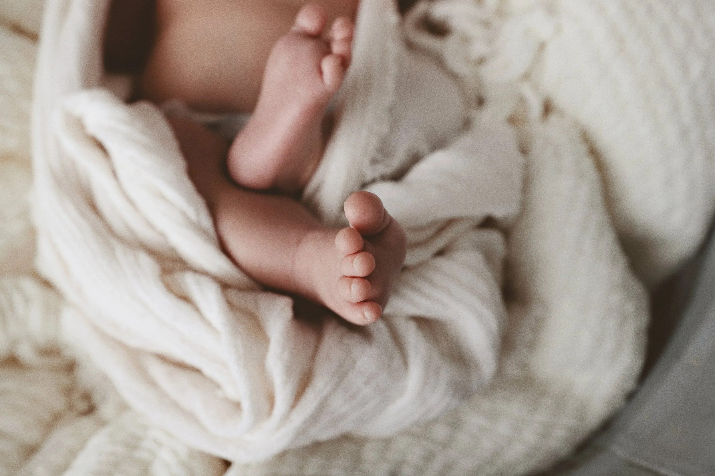 Close-up of a newborn baby sleeping, wrapped in a soft, cream-colored blanket.