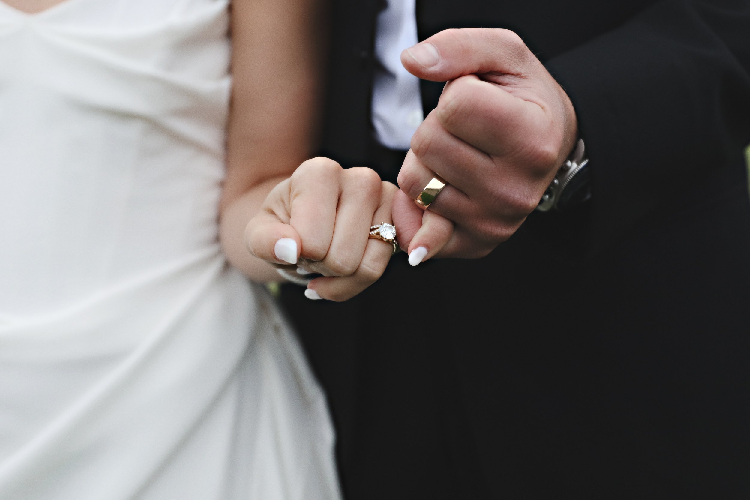 Close-up of a bride and groom holding hands, showing wedding rings; the bride's engagement ring and wedding band, and the groom's gold band.