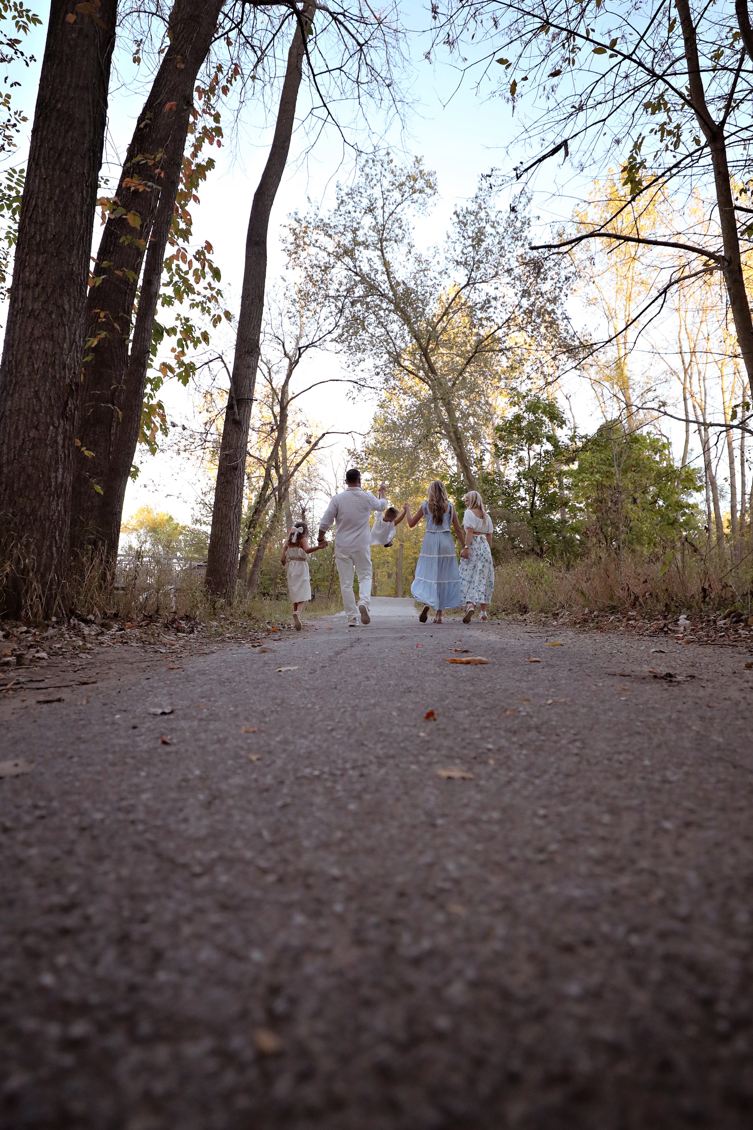 Family walking together on a wooded trail in the late afternoon, surrounded by trees with sparse leaves.