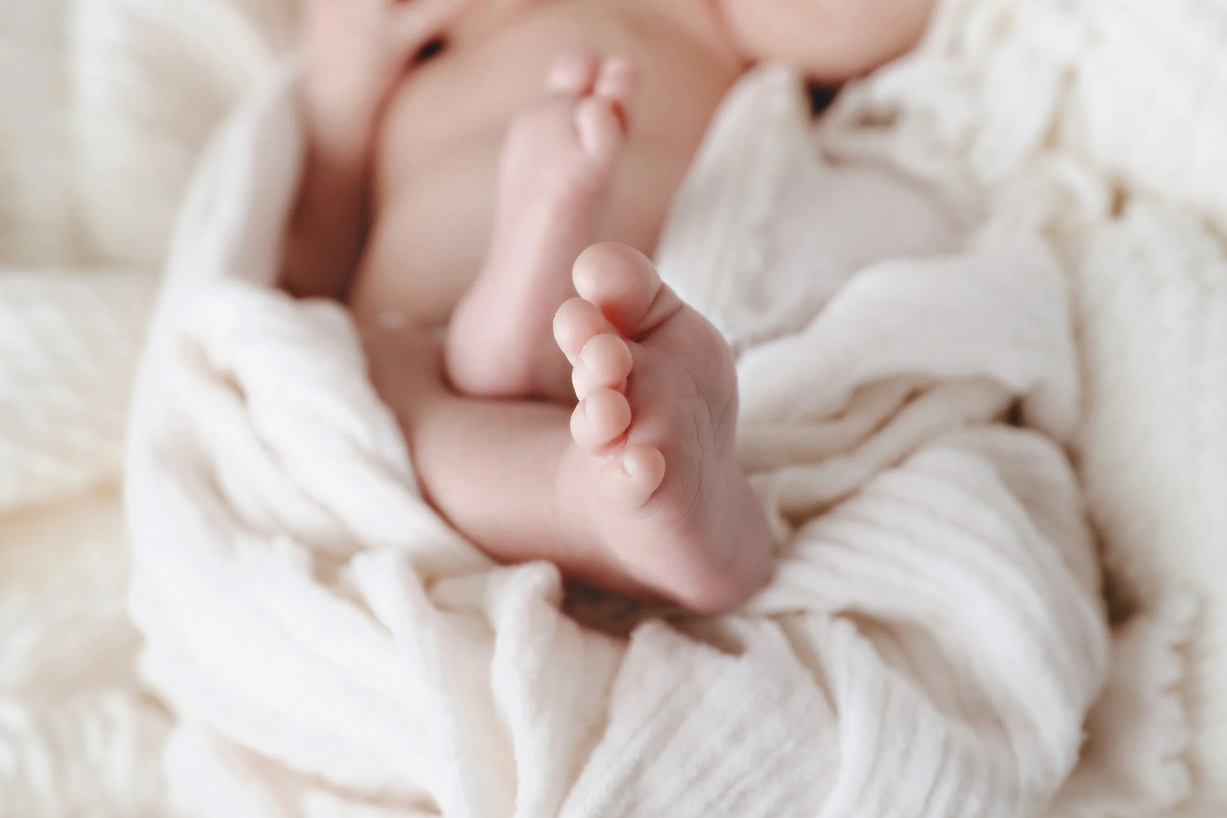 Close-up of a newborn baby's hand with fingers gently curled, resting on soft cream-colored fabric.
