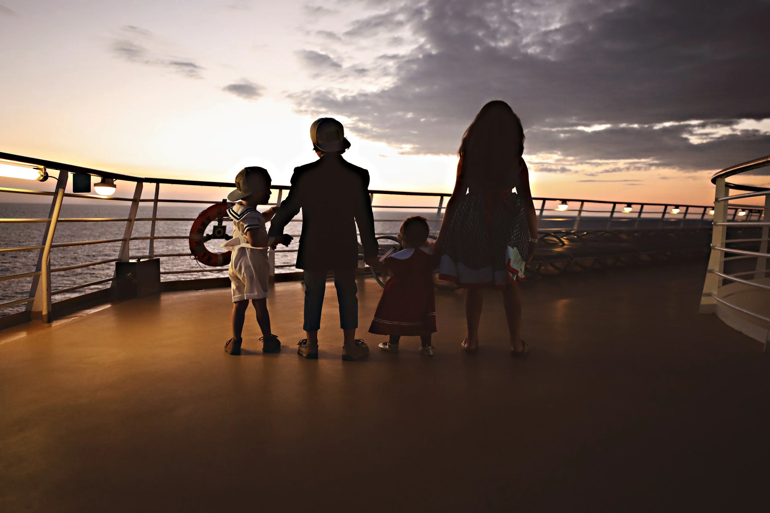 A family of five holding hands on a cruise ship deck at sunset.