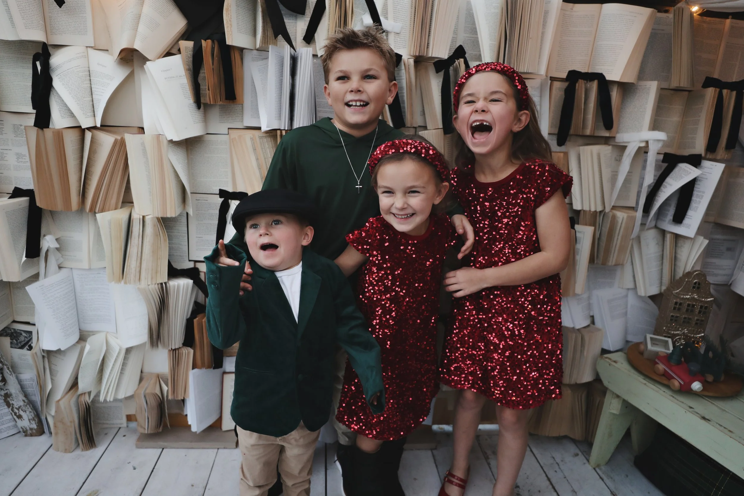 Four children standing in front of a wall decorated with open books tied with black ribbons, smiling and laughing.