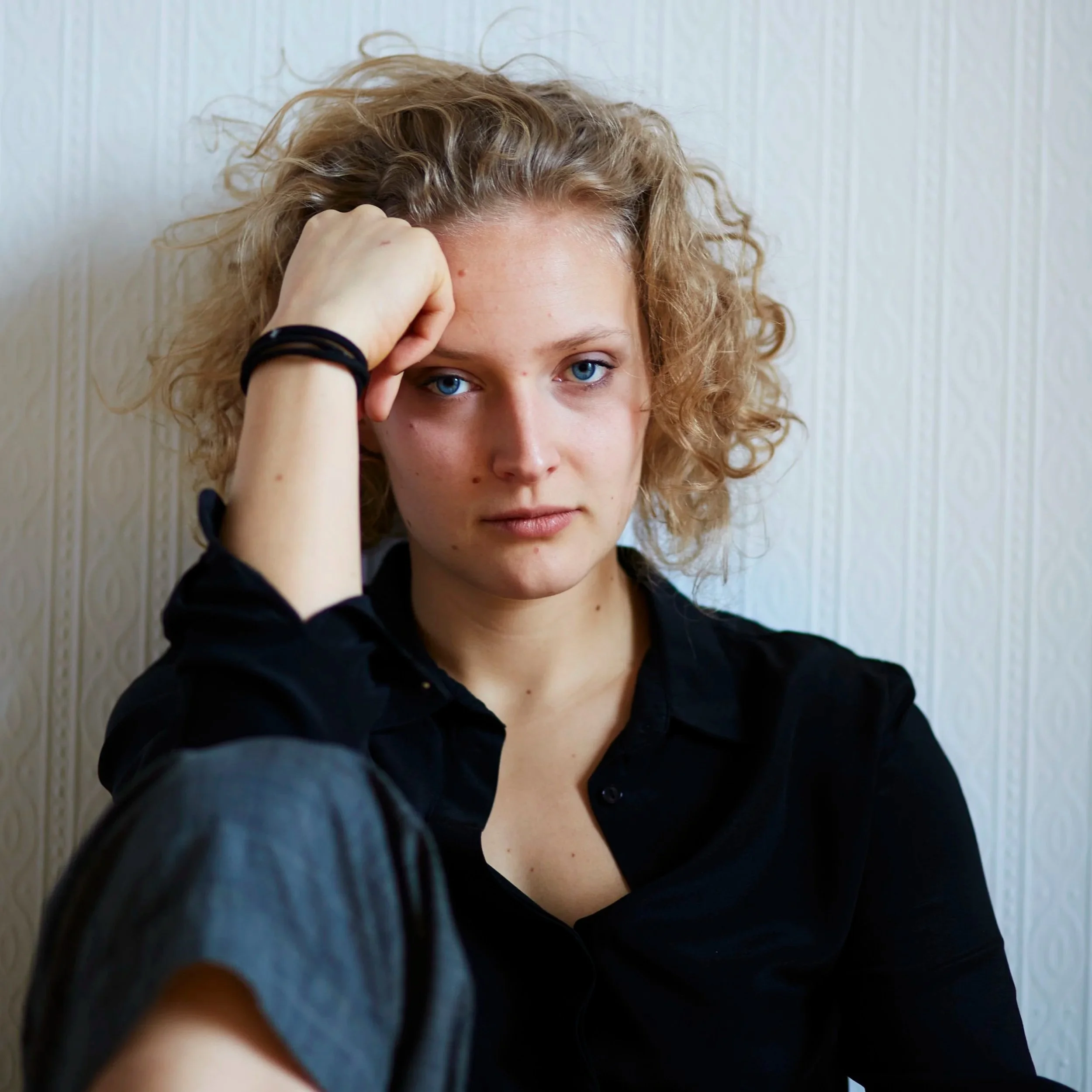 Nahaufnahme eines jungen Menschen mit blauen Augen und Locken, der die Kamera berührt.