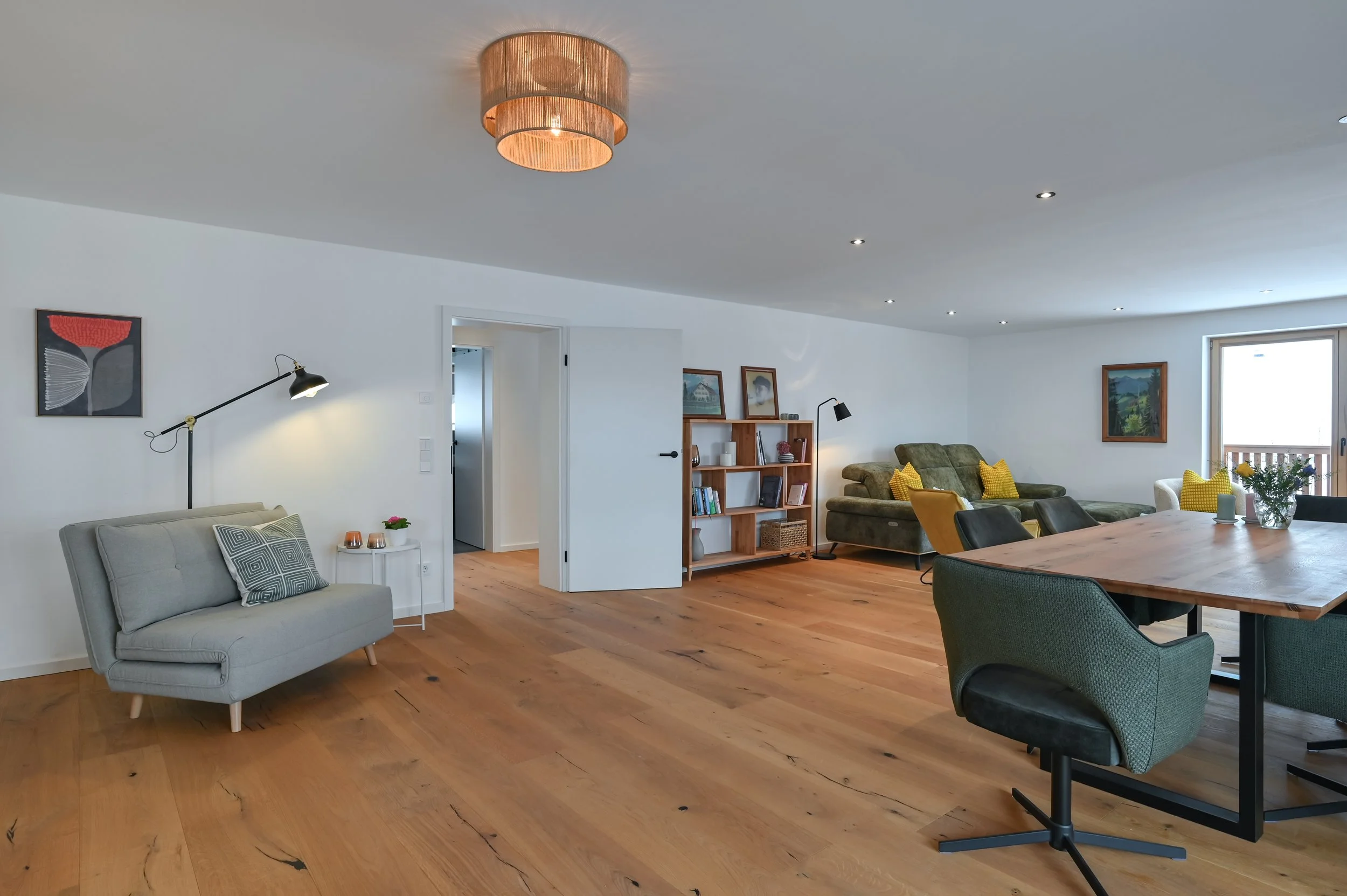 Offener Wohnbereich mit rustikalen Holzböden, weißen Wänden, mehreren Sofas, einem Esstisch mit Stühlen, Wandbildern und Stehlampen.