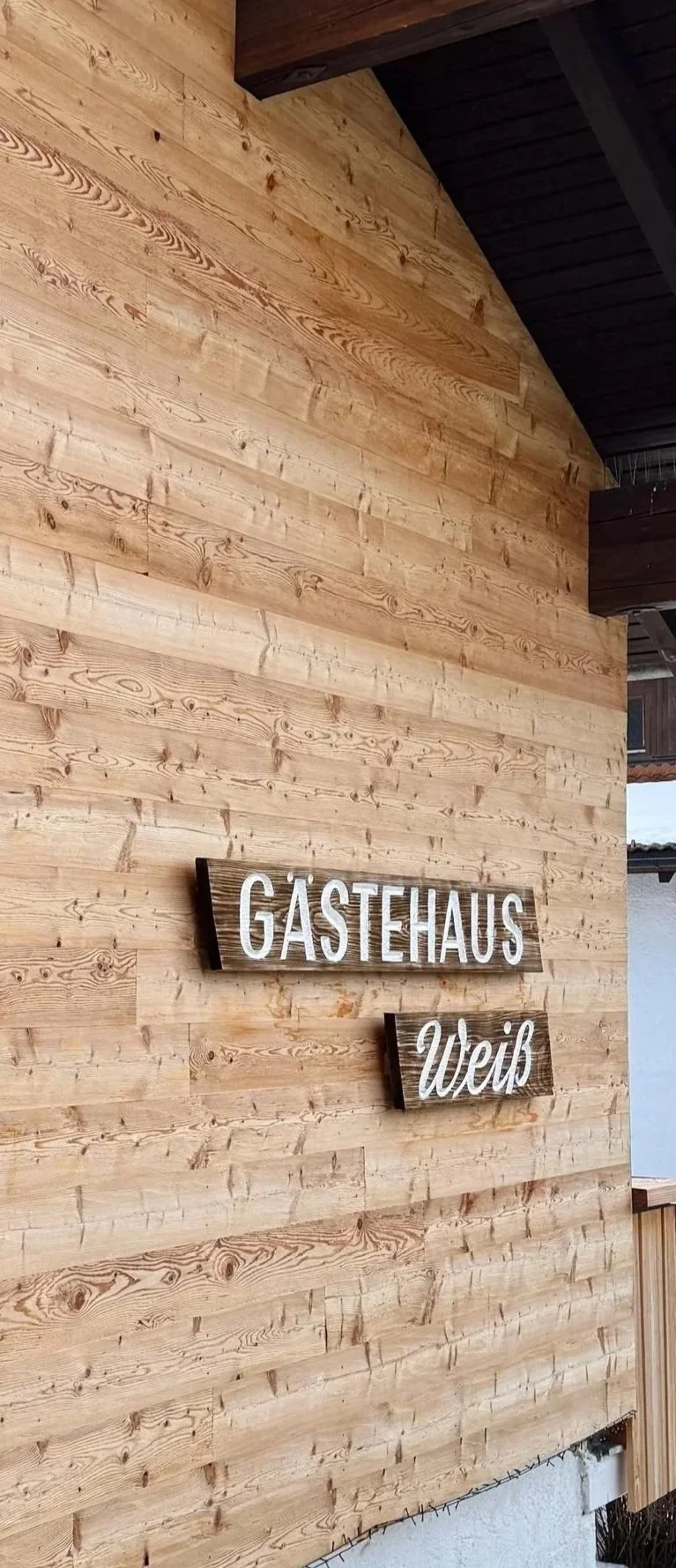 Holzverkleidung an einer Wand mit einem Schild, das 'GÄSTEHAUS Weiss' lautet.