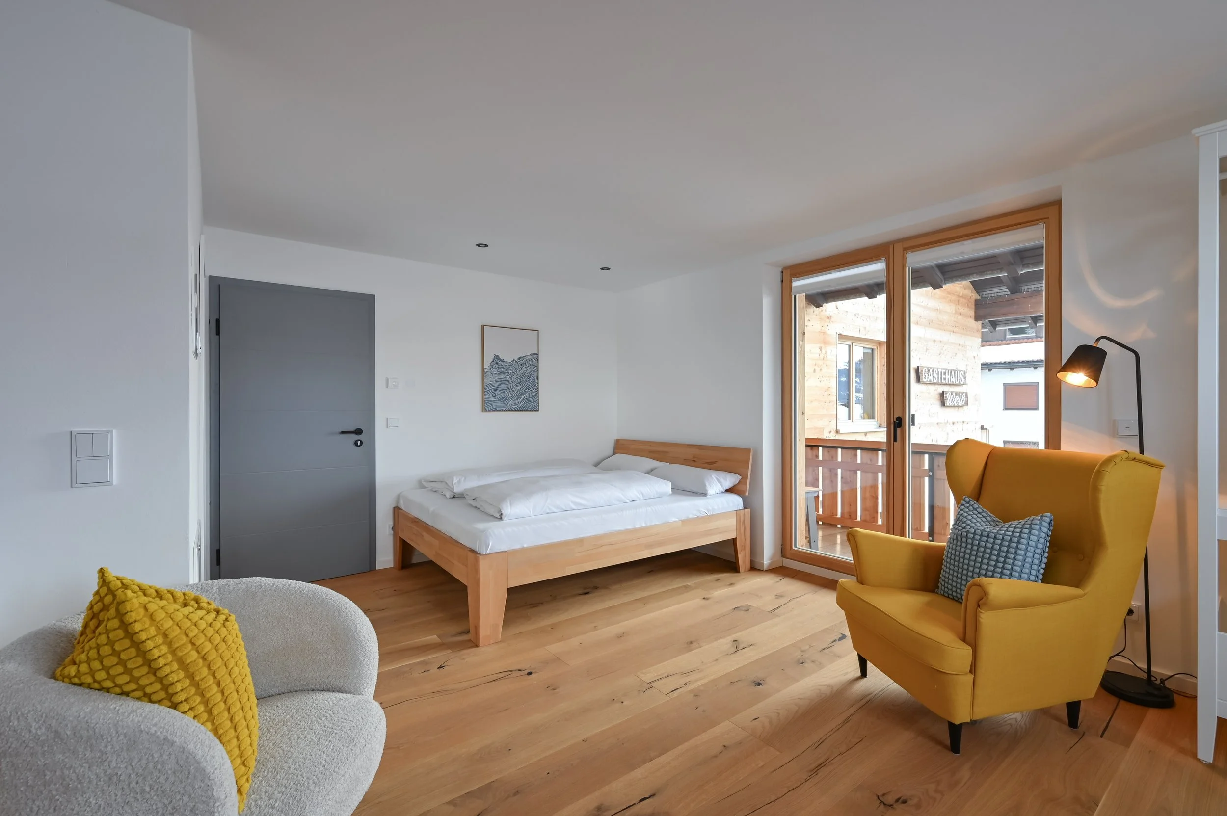 Modernes Apartment mit Holzfußboden, Doppelbett, großen Fenstern mit Balkon, gelbem Sessel, weißen und gelben Kissen, Wanddekoration.