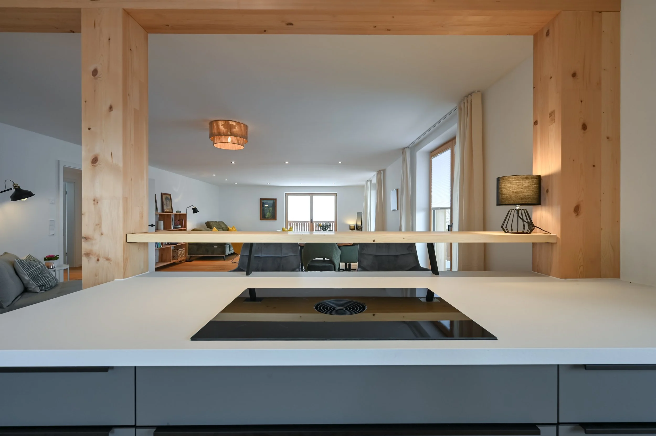 Moderne, offene Wohnung mit Küche im Vordergrund und Wohnzimmer im Hintergrund, große Fenster und schlichte Dekoration