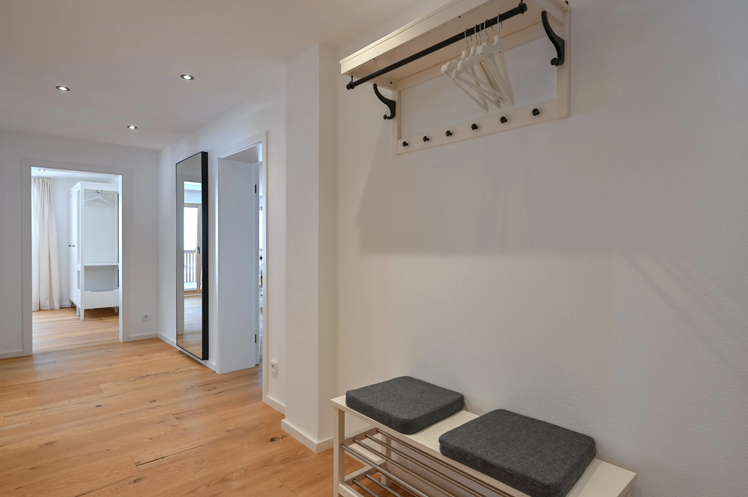 Flur mit Holzboden, Wandhaken, Sitzbank und durchsichtigen Vorhängen in einem hellen, modernen Haus.