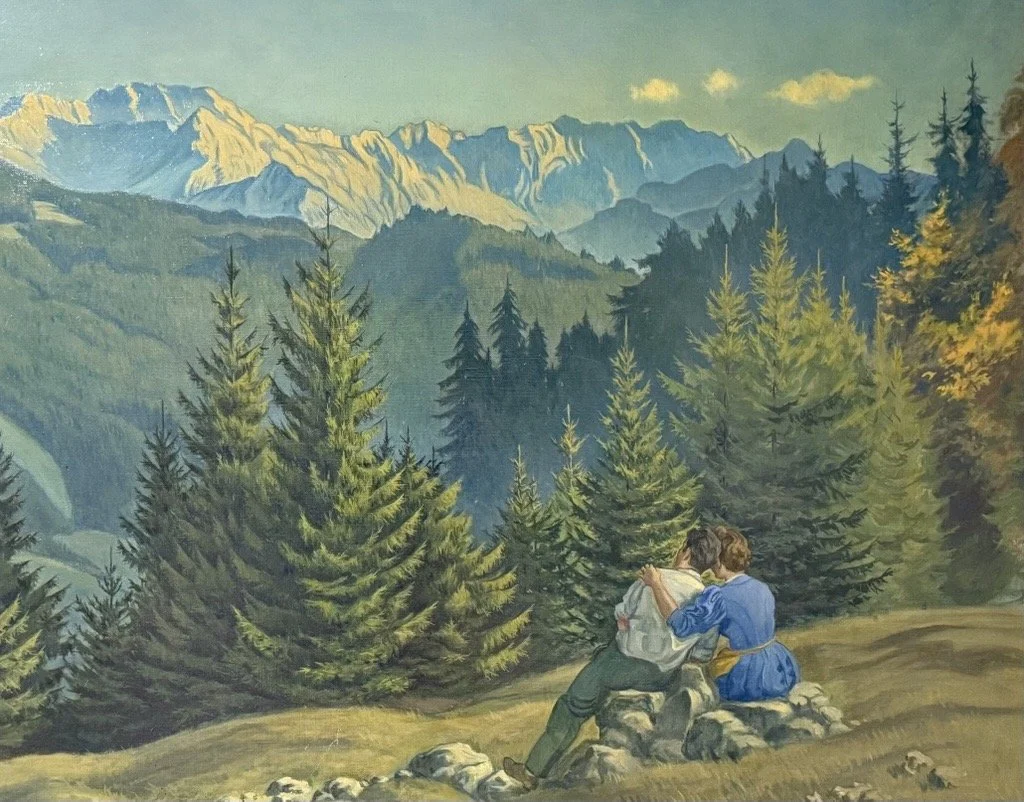 Ein Pärchen sitzt auf einem Felsen in einem Wald mit majestätischen Bergen im Hintergrund.