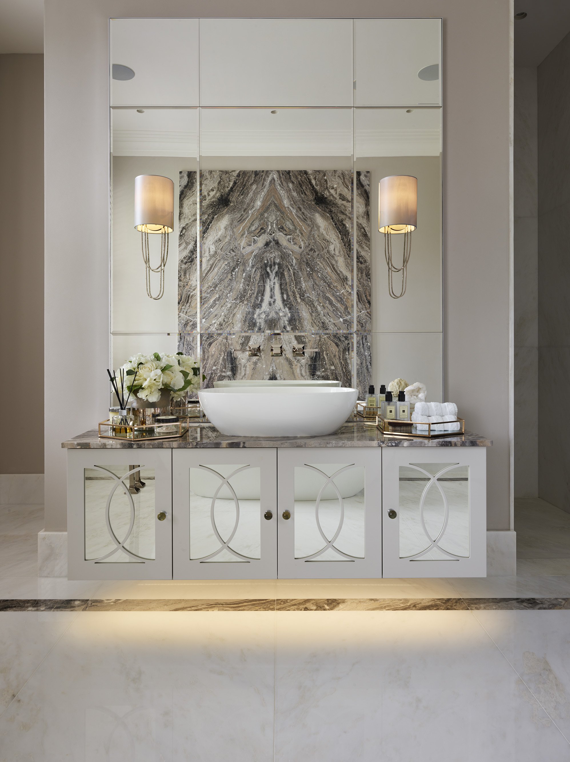 Modern bathroom vanity with white cabinet, marble countertop, vessel sink, large mirror, wall-mounted lights, and decorative accessories.