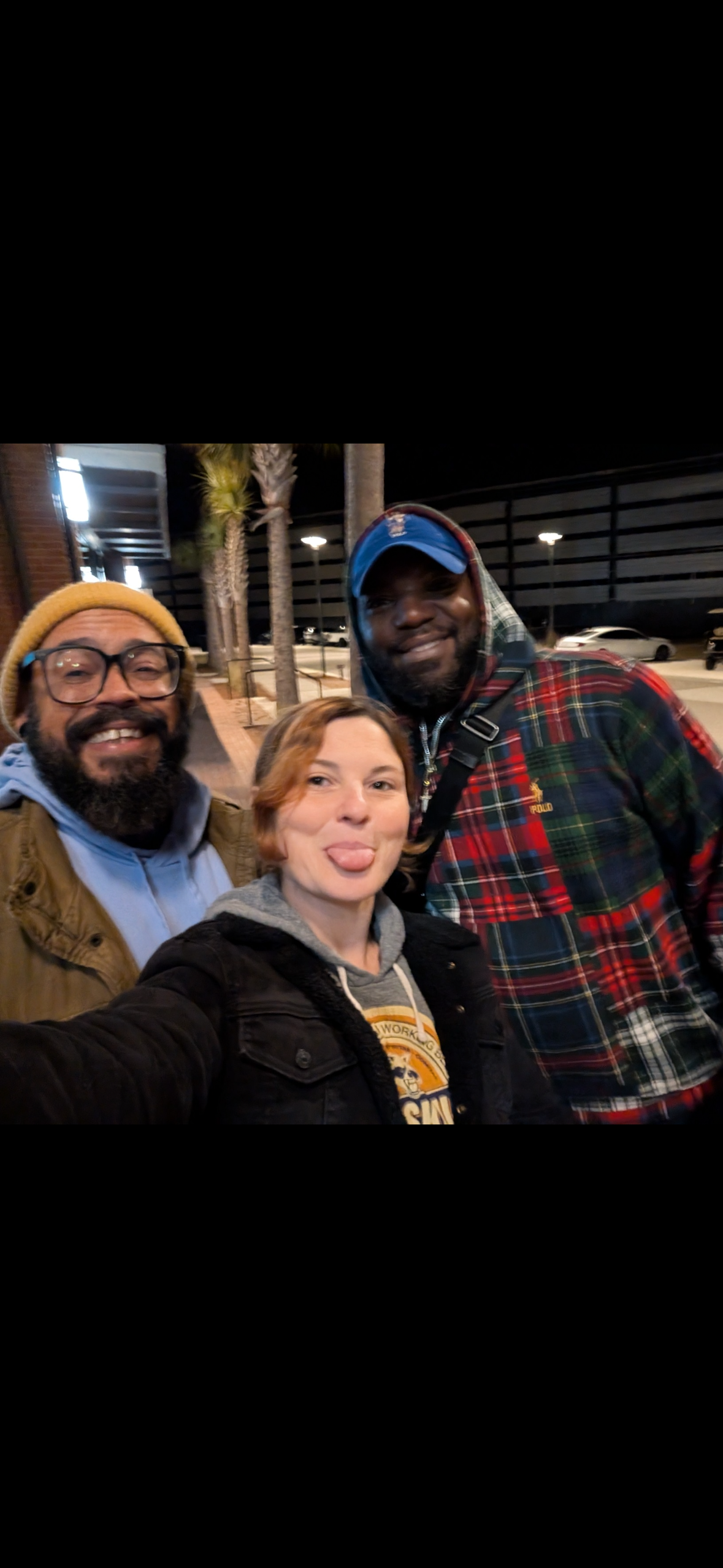 Three friends taking a selfie at night outdoors, smiling and making funny faces.