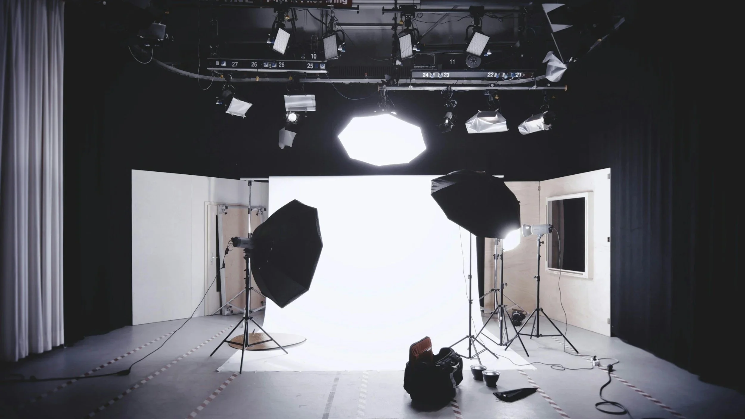 Photography studio with large white backdrop, professional lighting equipment, and black curtains on sides.