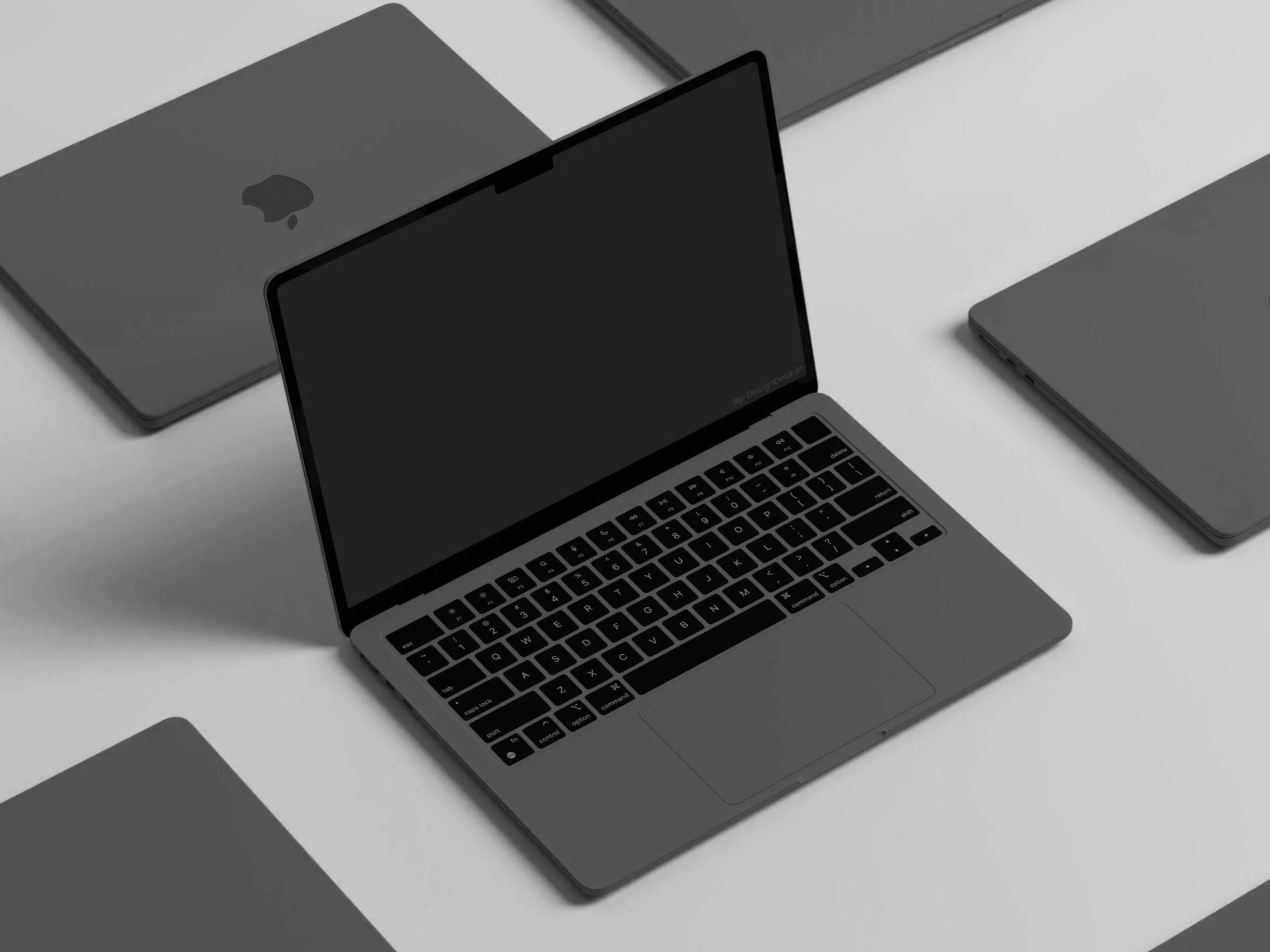 Top view of a modern silver laptop with a black keyboard on a white surface, surrounded by other closed laptops in different shades of gray.