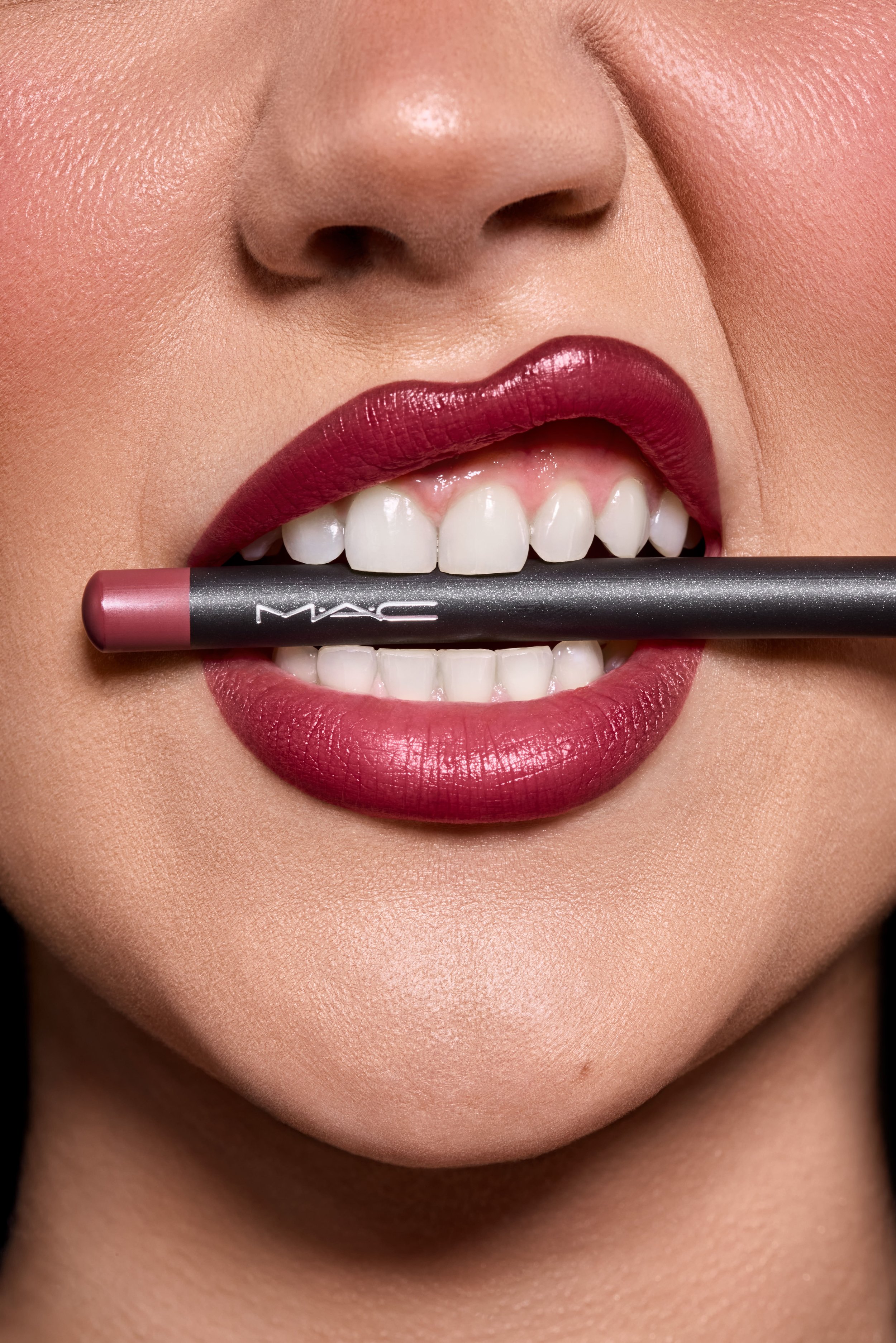 Nahaufnahme eines Frauenchens mit roten Lippen, das einen Lippenstift von MAC zwischen den Zähnen hält.