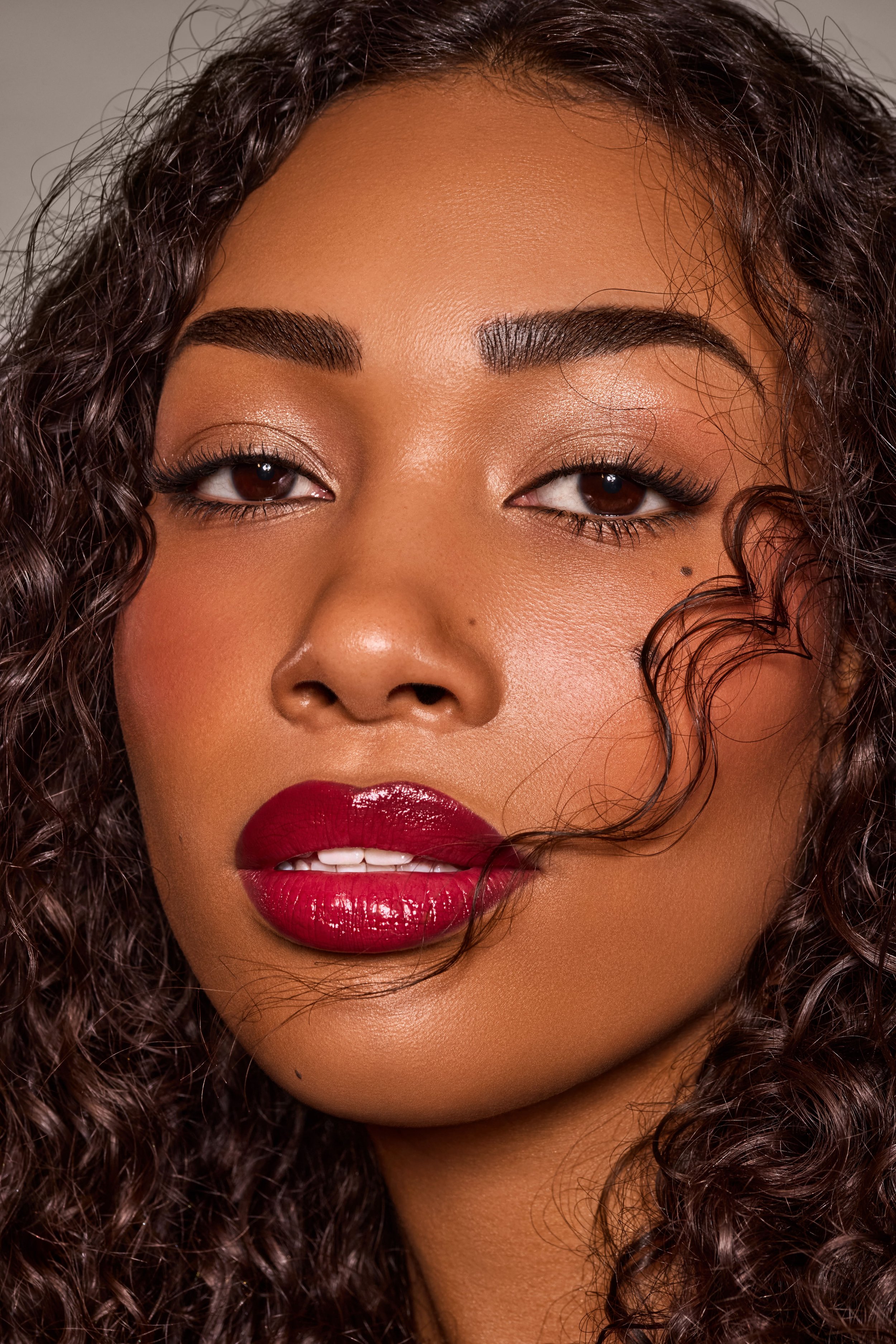 Nahaufnahme eines Models mit dunklem Teint, lockigem Haar, roten Lippen und dezentem Make-up.