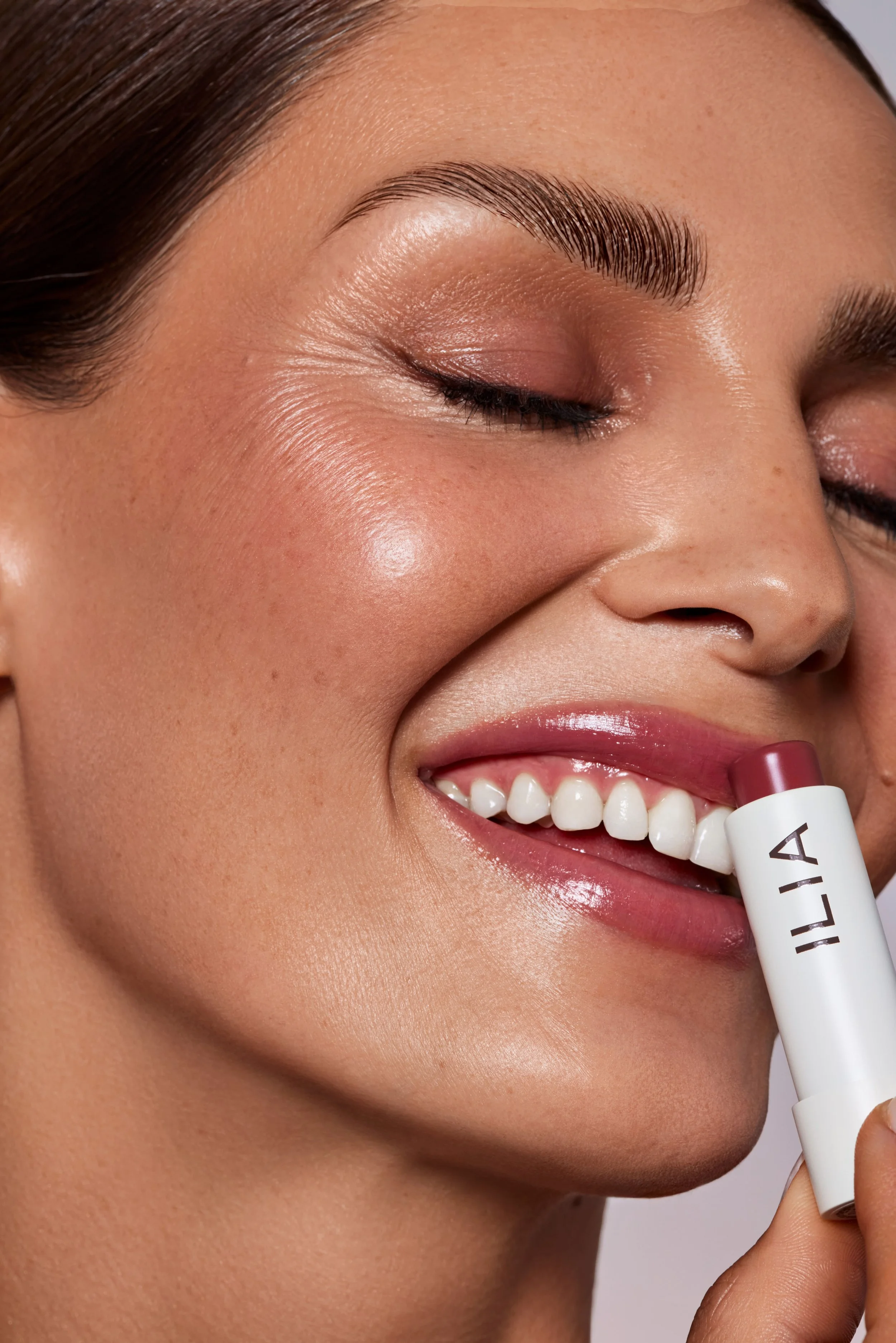 Nahaufnahme eines lachenden Mädchens mit weicher Haut, das einen Lippenbalsam hält.