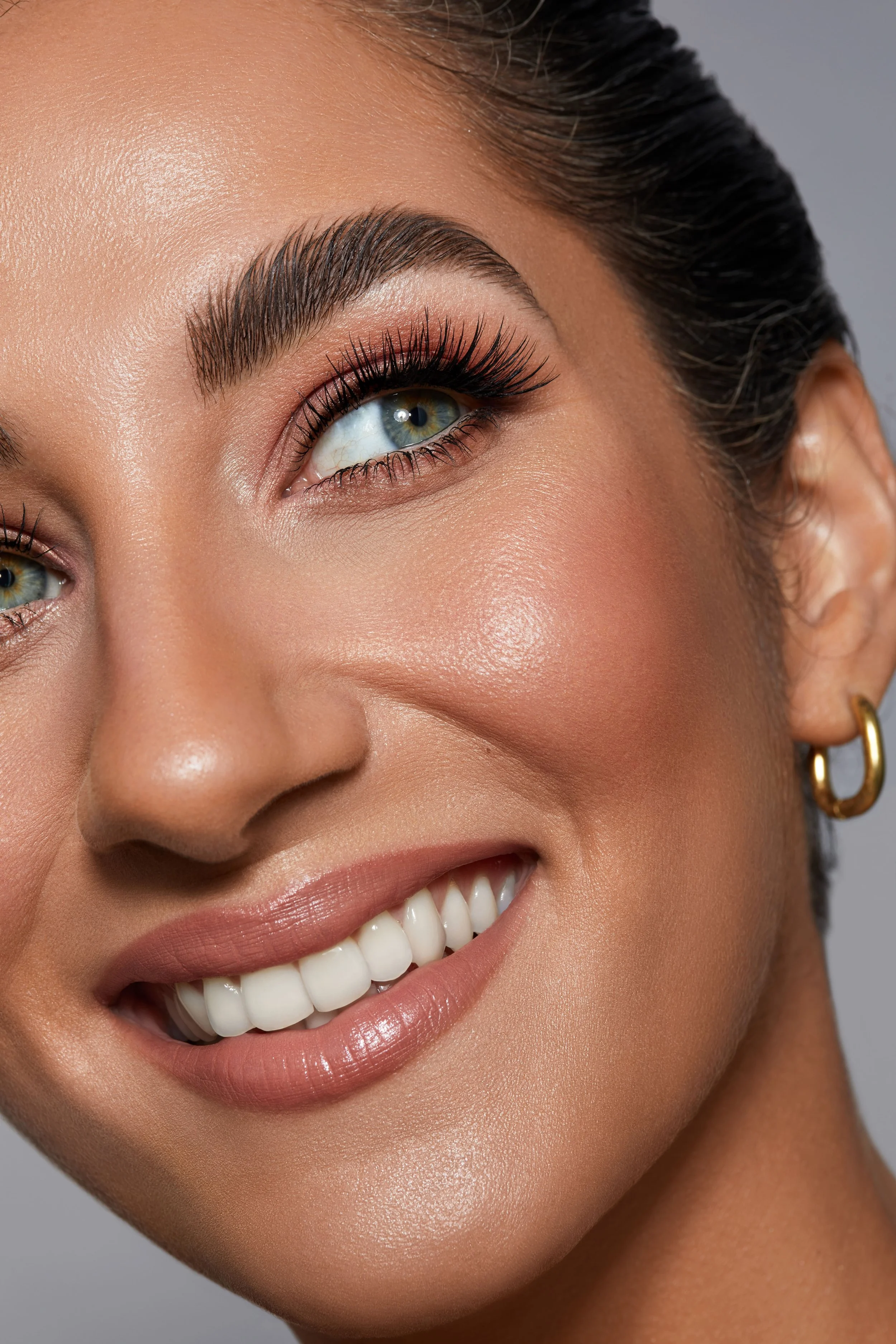 Nahaufnahme eines lachenden Frauenporträts mit make-up, dunklem Haar und Goldohrring.