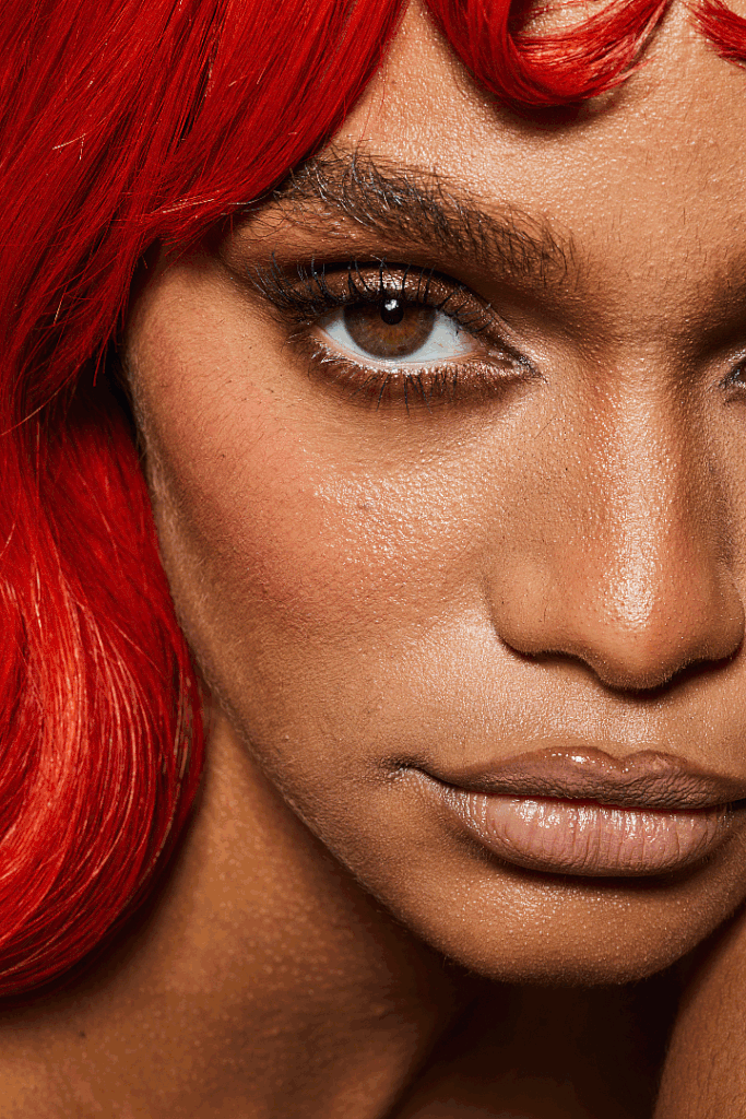 Nahaufnahme eines Gesichts mit roten Haaren, braunen Augen, glamourösem Make-up und natürlicher Hauttextur.