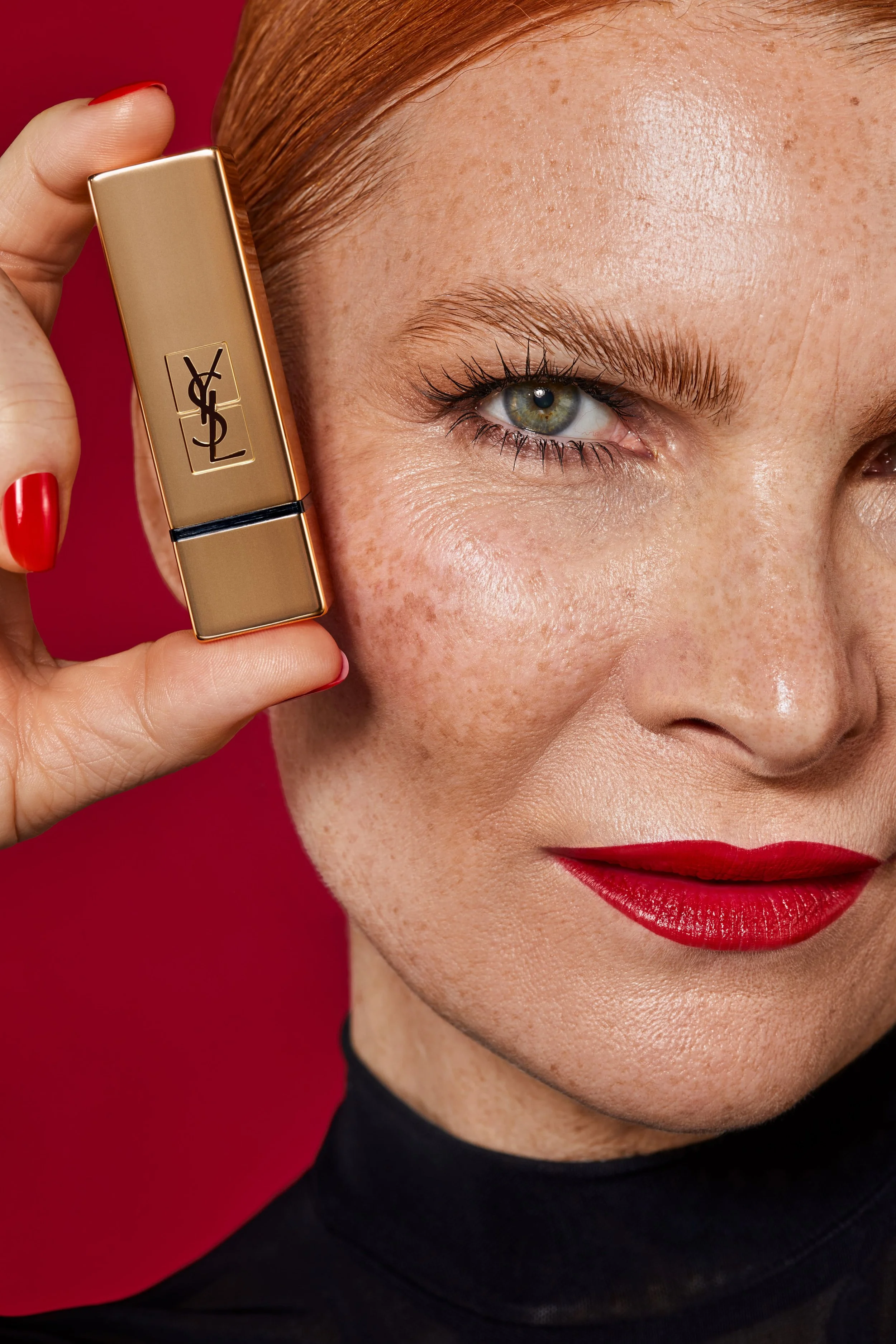Nahaufnahme eines Modells mit rotem Lippenstift, das YSL-Make-upprodukt hält, vor rotem Hintergrund.