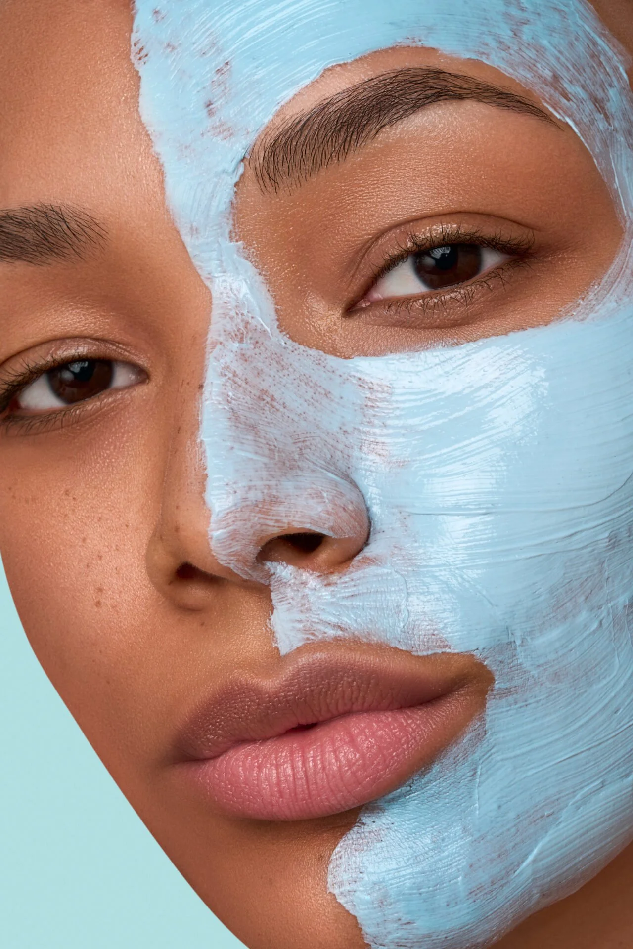 Nahaufnahme eines Gesichts mit Hälfte der Haut sichtbar und der anderen Hälfte mit einer weißen Gesichtsmaske bedeckt.