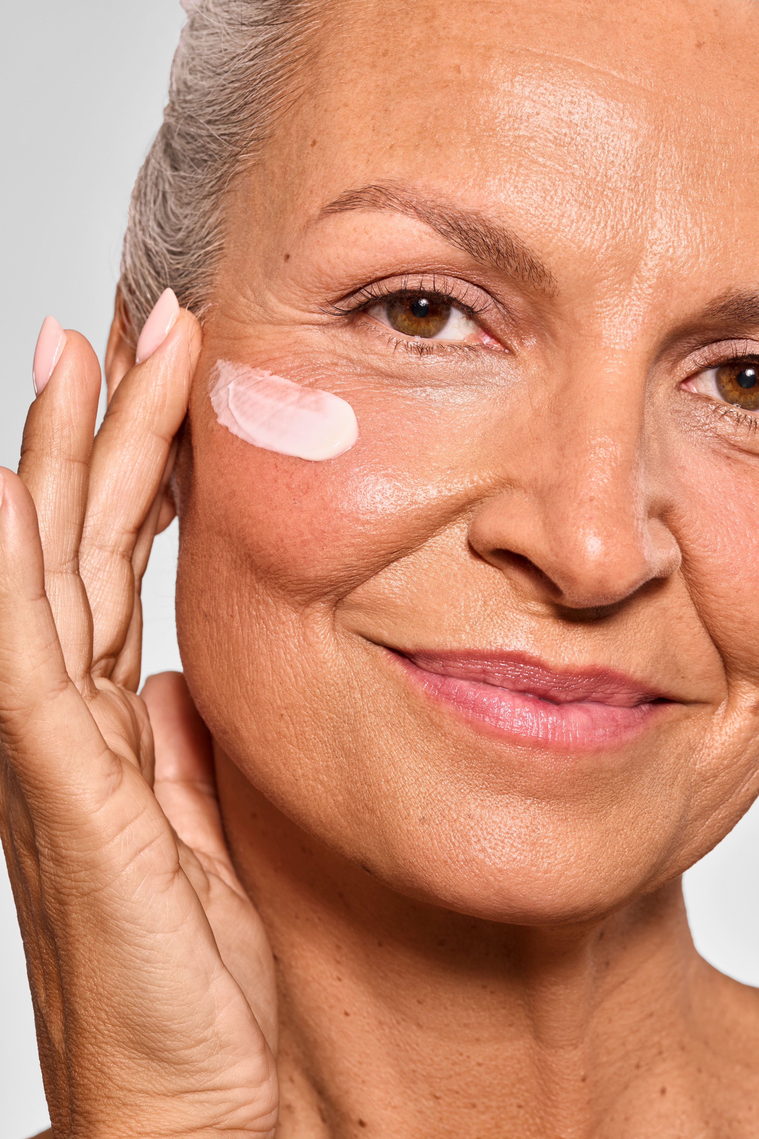 Nahaufnahme eines älteren Mädchens, das Hautcreme auf die Wange aufträgt und lächelt.