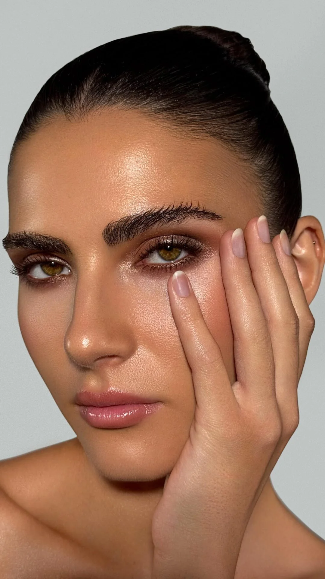 Nahaufnahme eines Mädchens mit dunklem Haar, braunen Augen und gepflegter Haut, das mit einer Hand ihr Gesicht berührt.