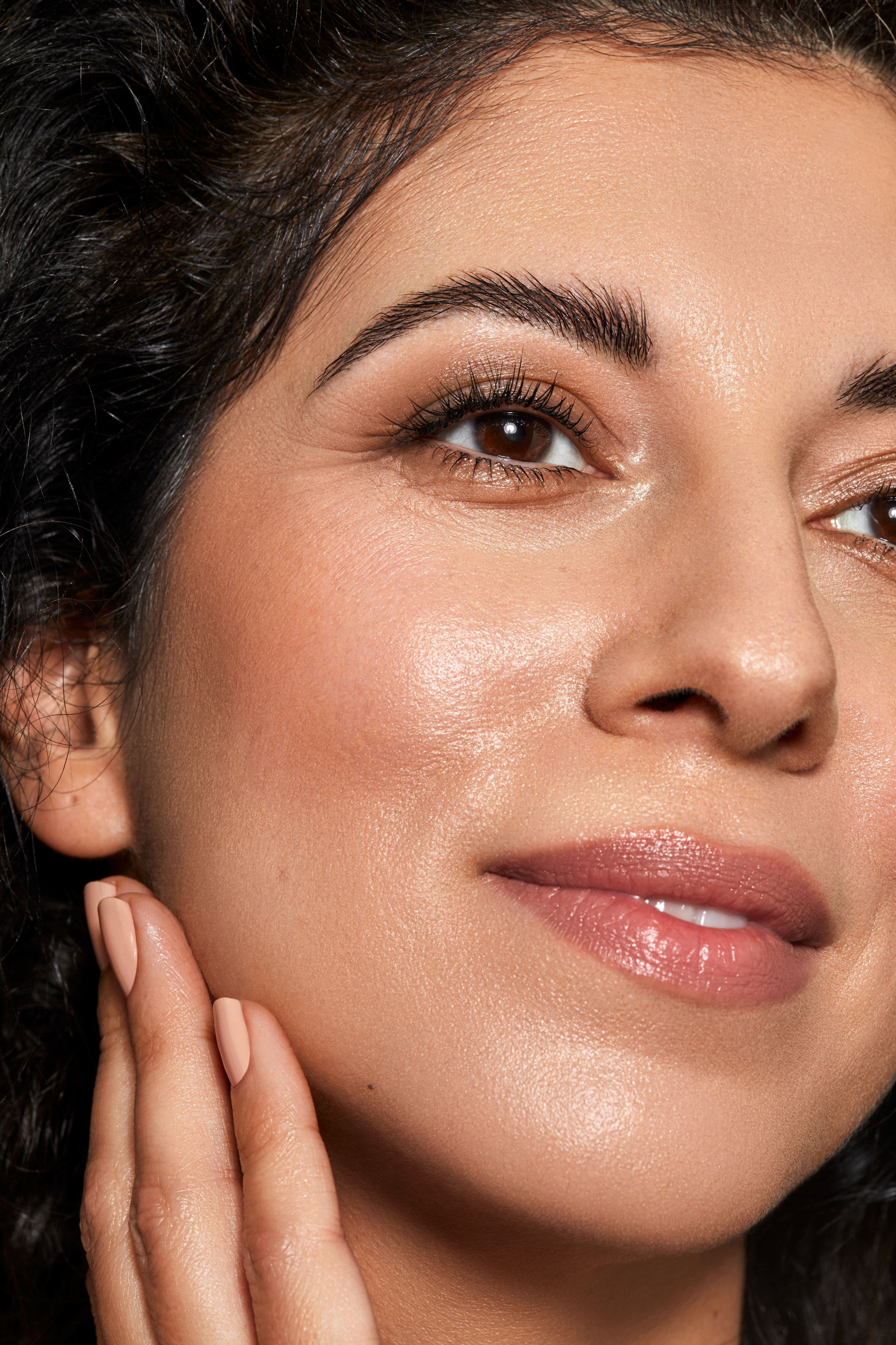 Nahaufnahme eines lächelnden Frauengesichts mit natürlichem Make-up, glatter Haut und dunklen Locken.