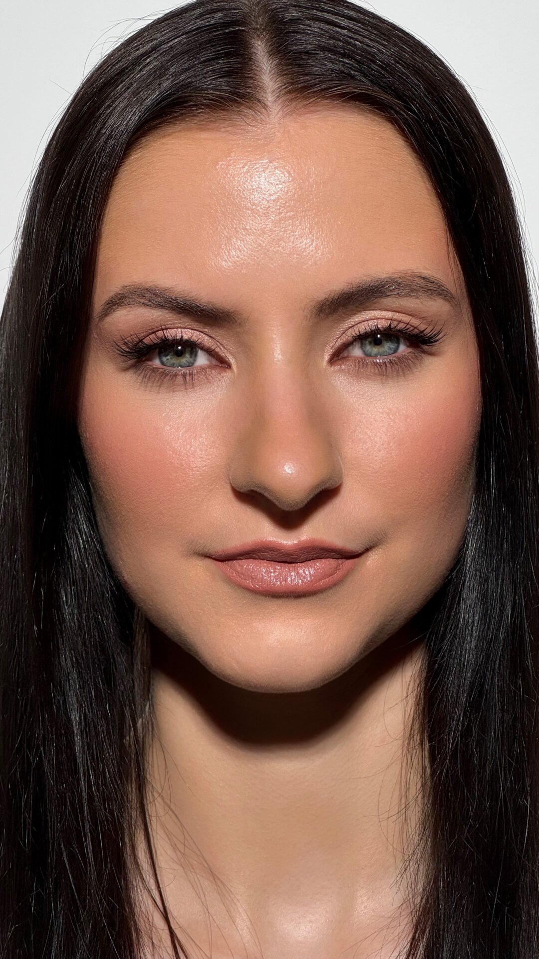 Nahaufnahme eines Frauengesichts mit dunklen Haaren, grünen Augen, natürlichem Make-up und neutralem Hintergrund.