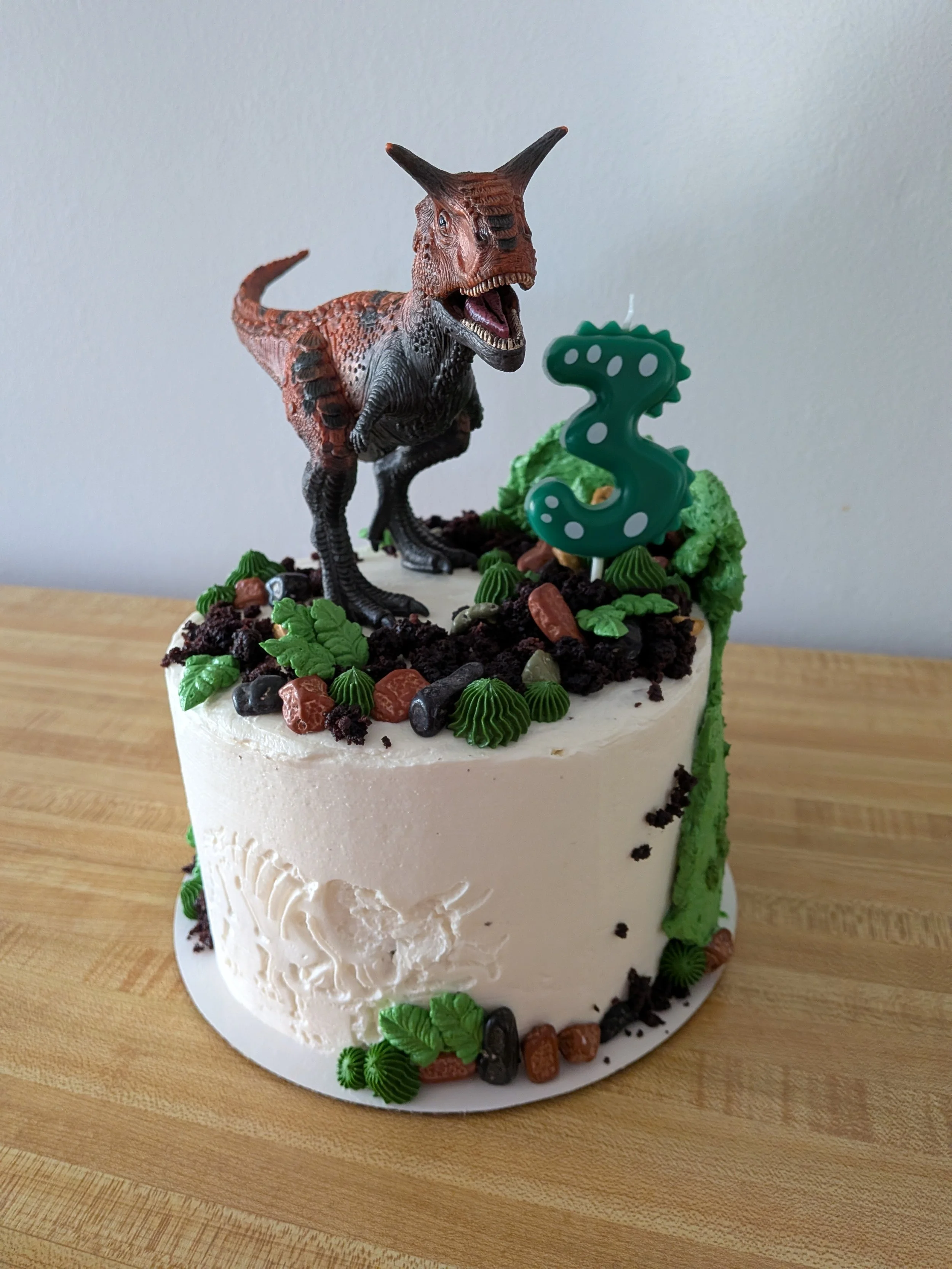 Dinosaur themed birthday cake with a dinosaur figure and a number 3 candle on top.