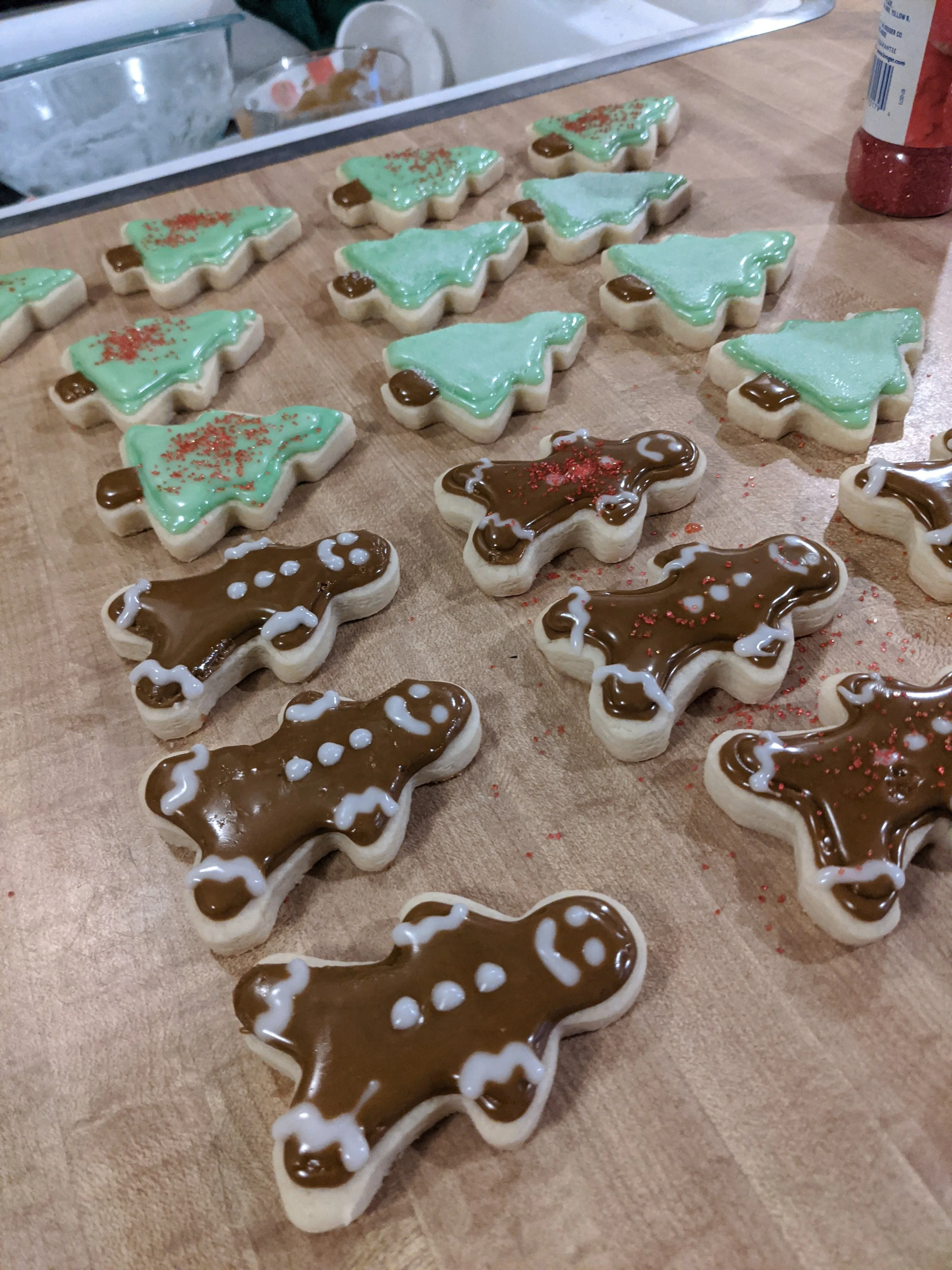 Christmas tree shaped sugar cookies decorated with green and brown icing, some with red sprinkles, laid on a wooden surface.
