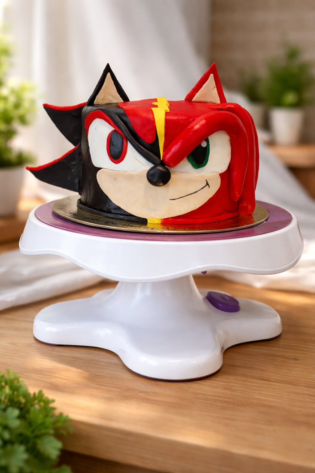Cake shaped like Sonic the Hedgehog's face, with half black and half red, on a white cake stand.