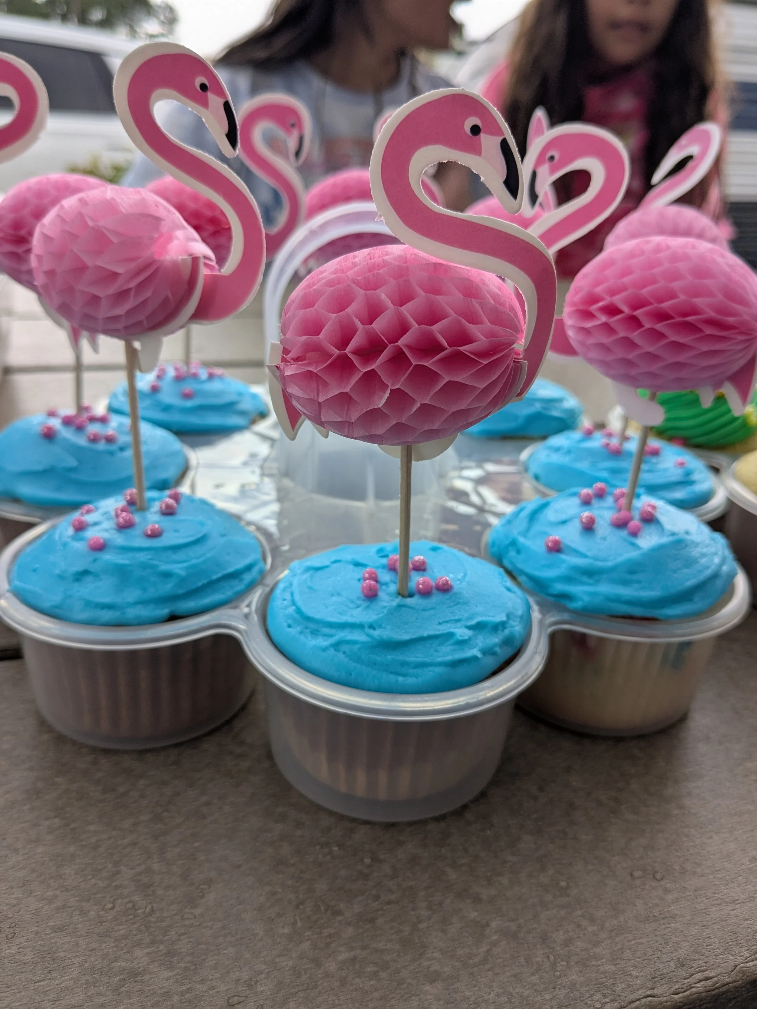 Cupcakes with blue frosting and pink flamingo decorations on sticks.