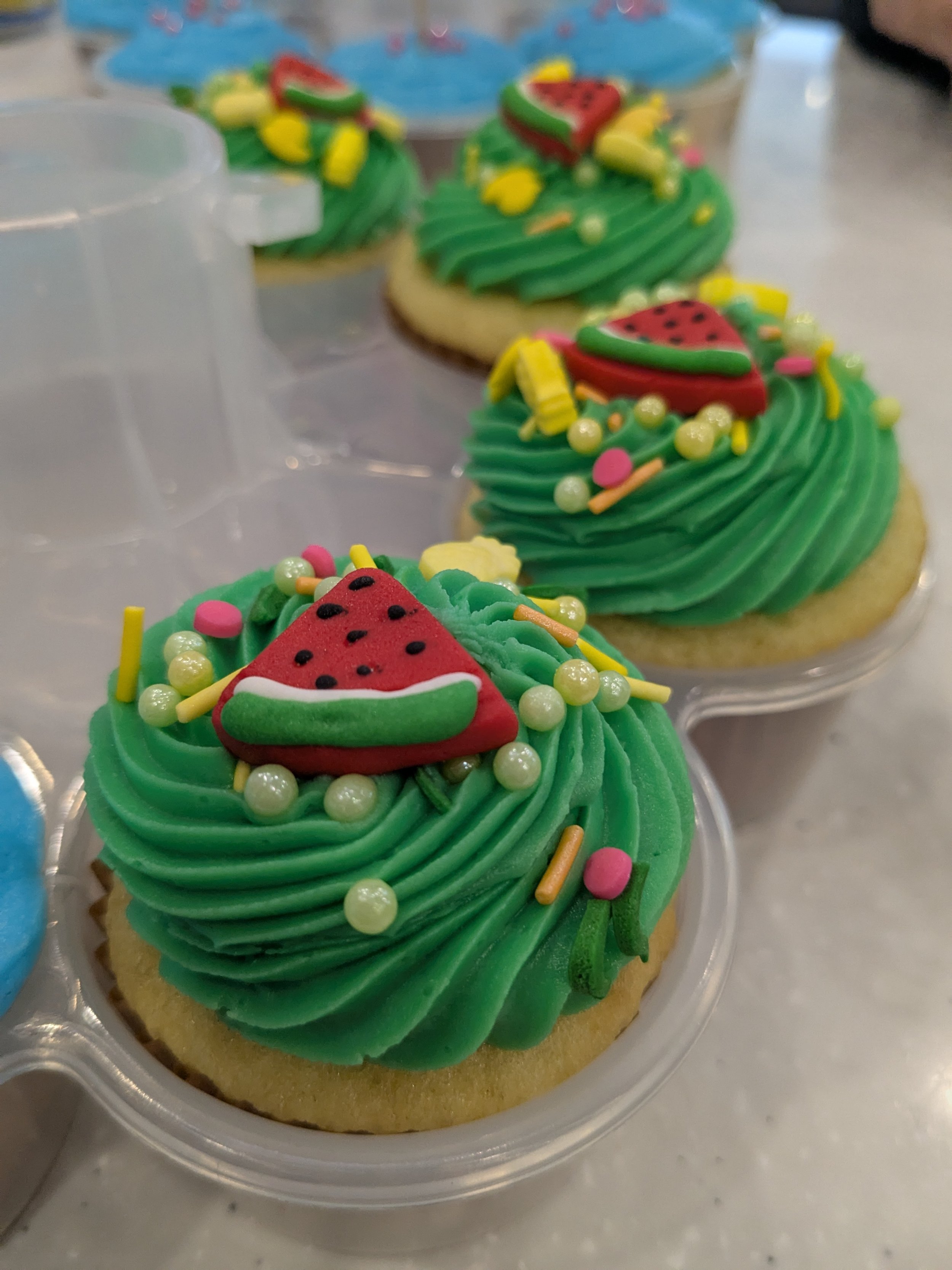 Close-up of decorated cookies with green icing, strawberry-shaped toppers, and colorful sprinkles.
