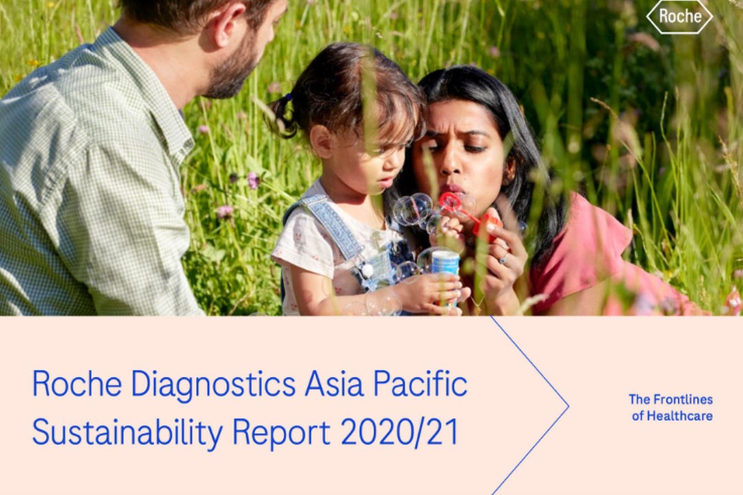 A family of three outdoors in a grassy field, blowing bubbles together. The man is wearing a light green shirt, the woman is in pink, and the young girl is in denim overalls.