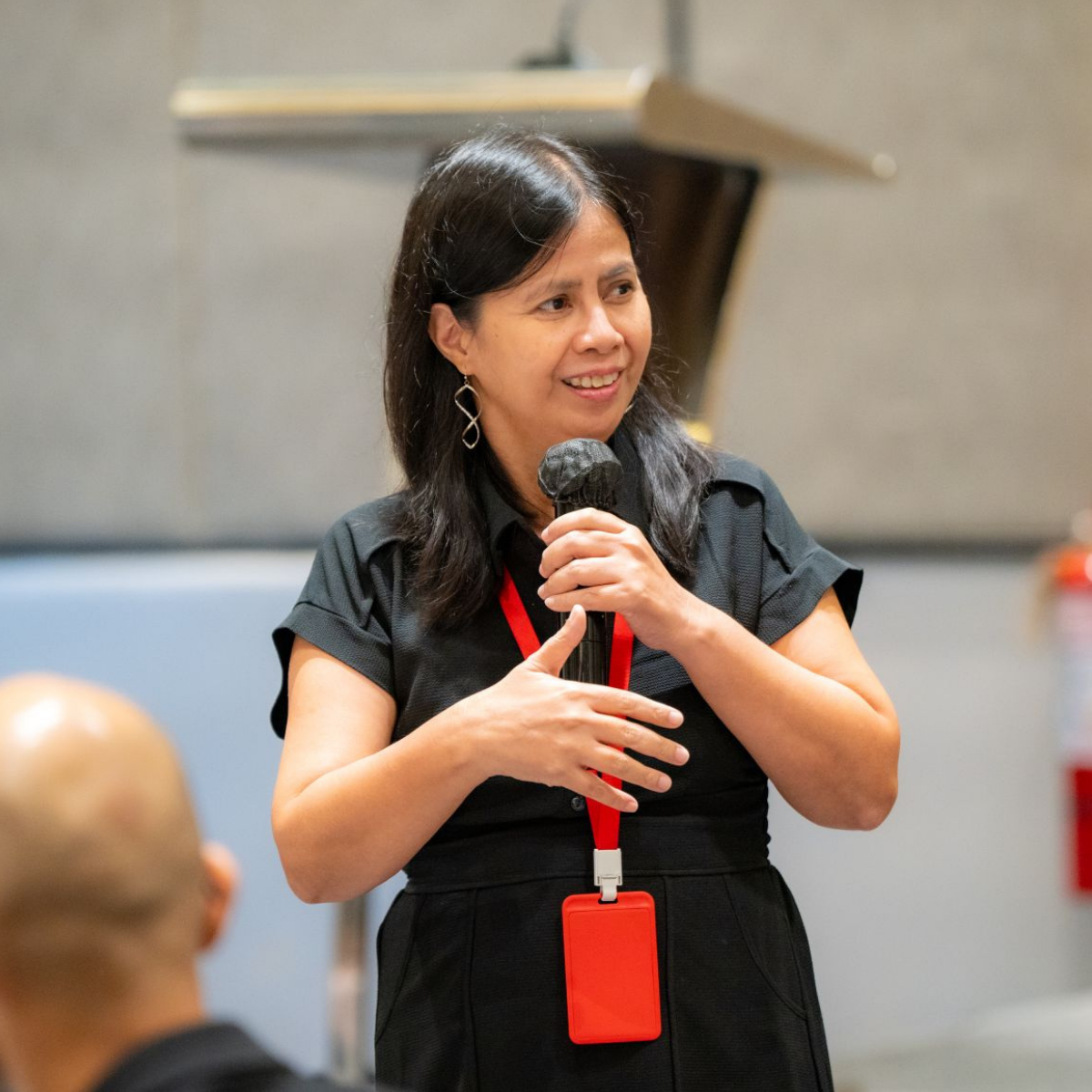 Woman speaking into a microphone during a presentation or event in an indoor setting.