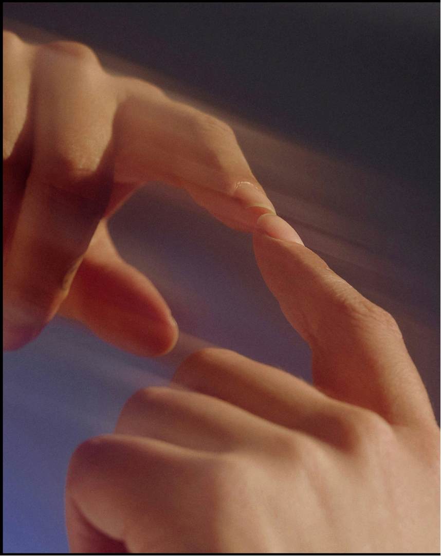 Close-up of two hands with fingers touching, forming a delicate shape against a dark background.