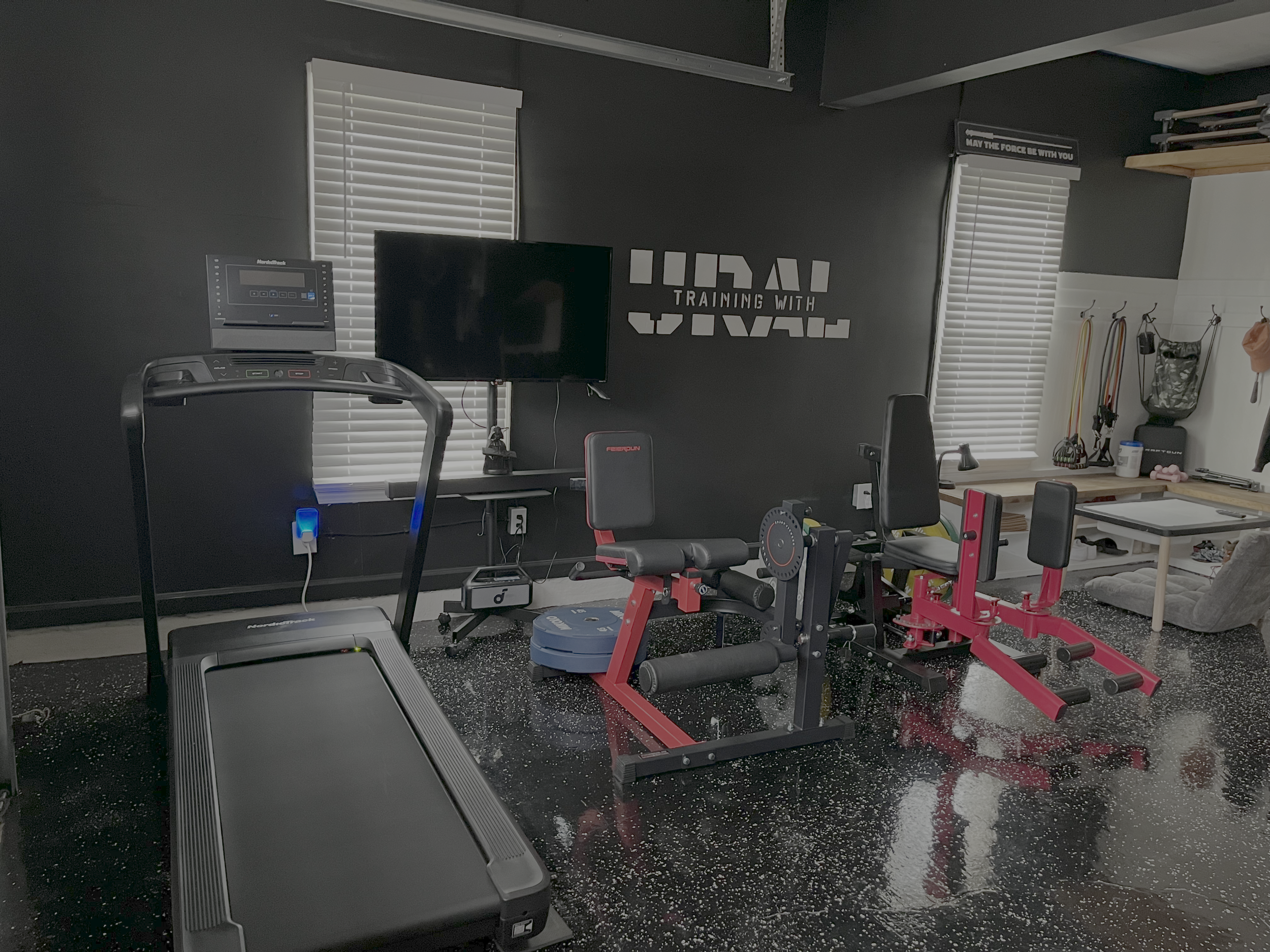 Home gym with treadmill, weight bench, and exercise equipment in a room with a TV on the wall.