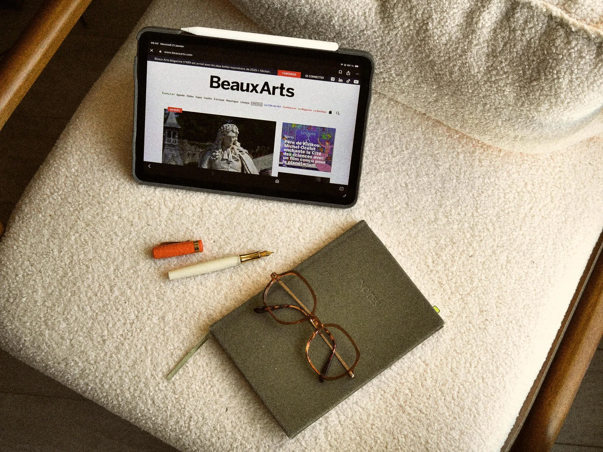 Une tablette, un stylo à plume, un cahier, une paire de lunettes et un crayon-orange sur une surface beige