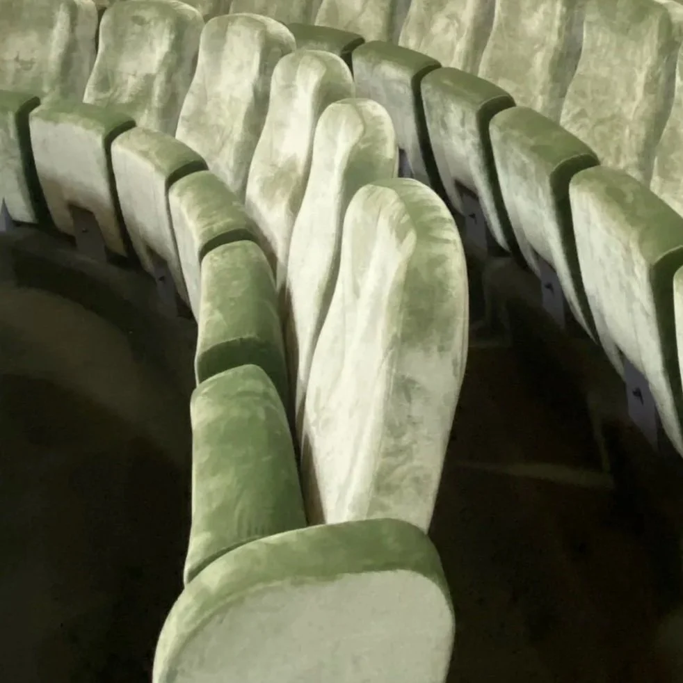 Des sièges d'une salle de cinéma ou théâtre en velours vert foncé, disposés en rangée curve.