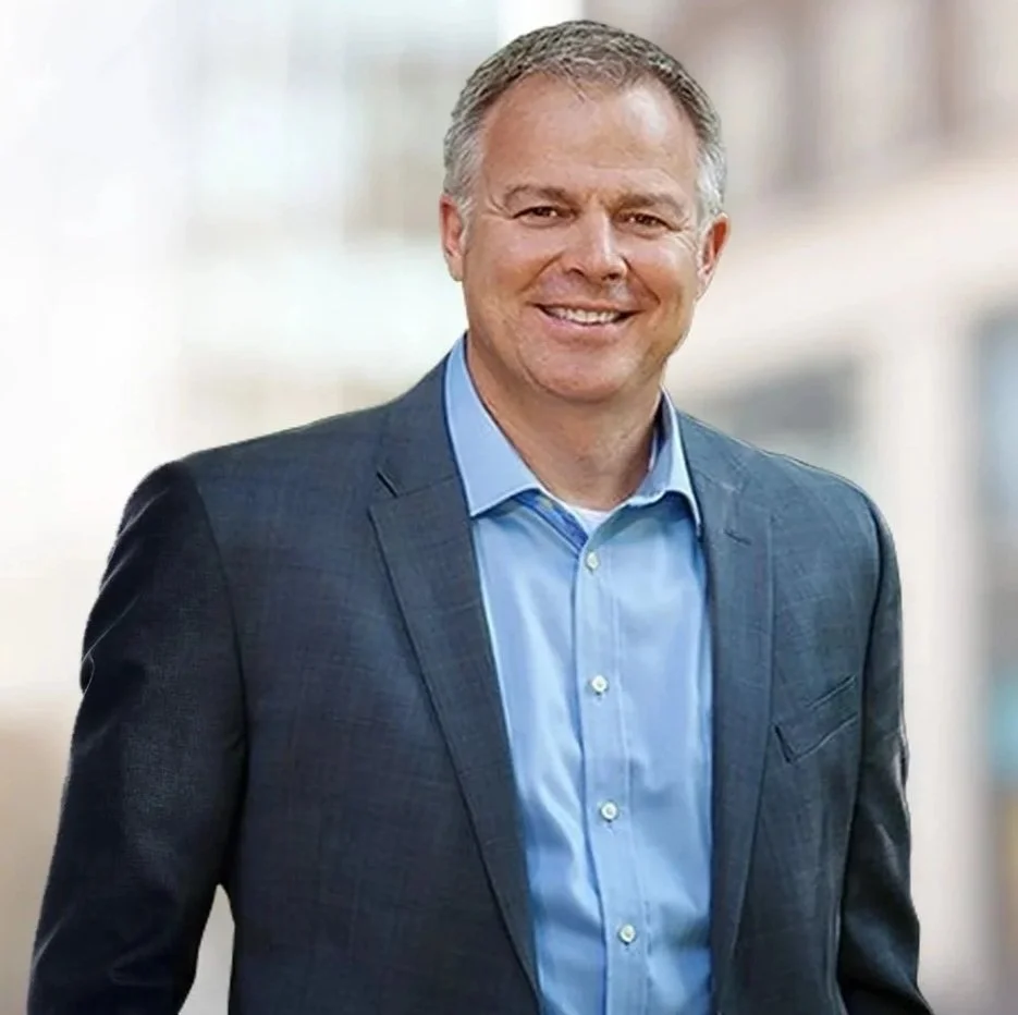 Smiling man in a blue suit and light blue shirt standing outdoors