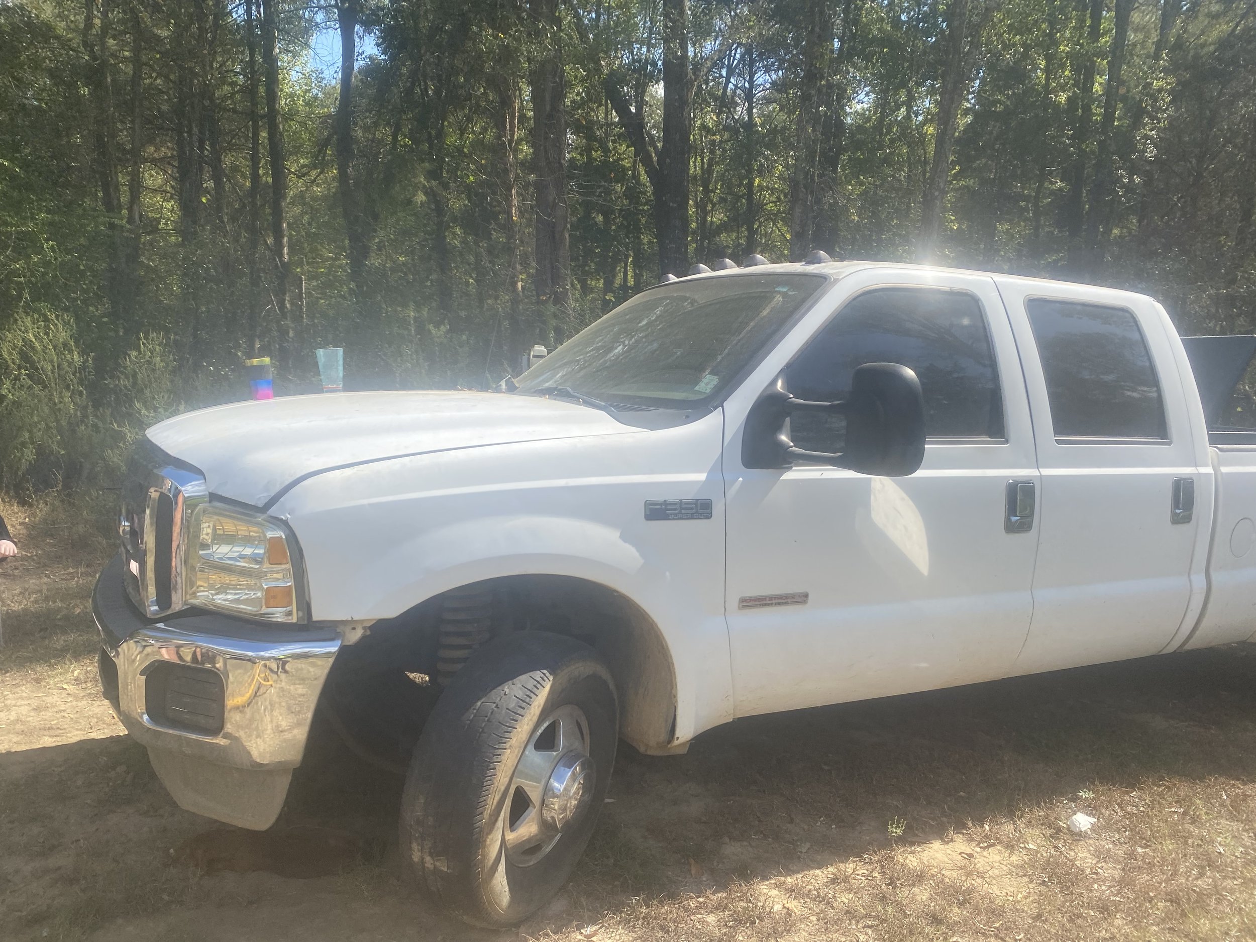 White Ford F-350 pickup truck parked on dirt ground with trees in the background.