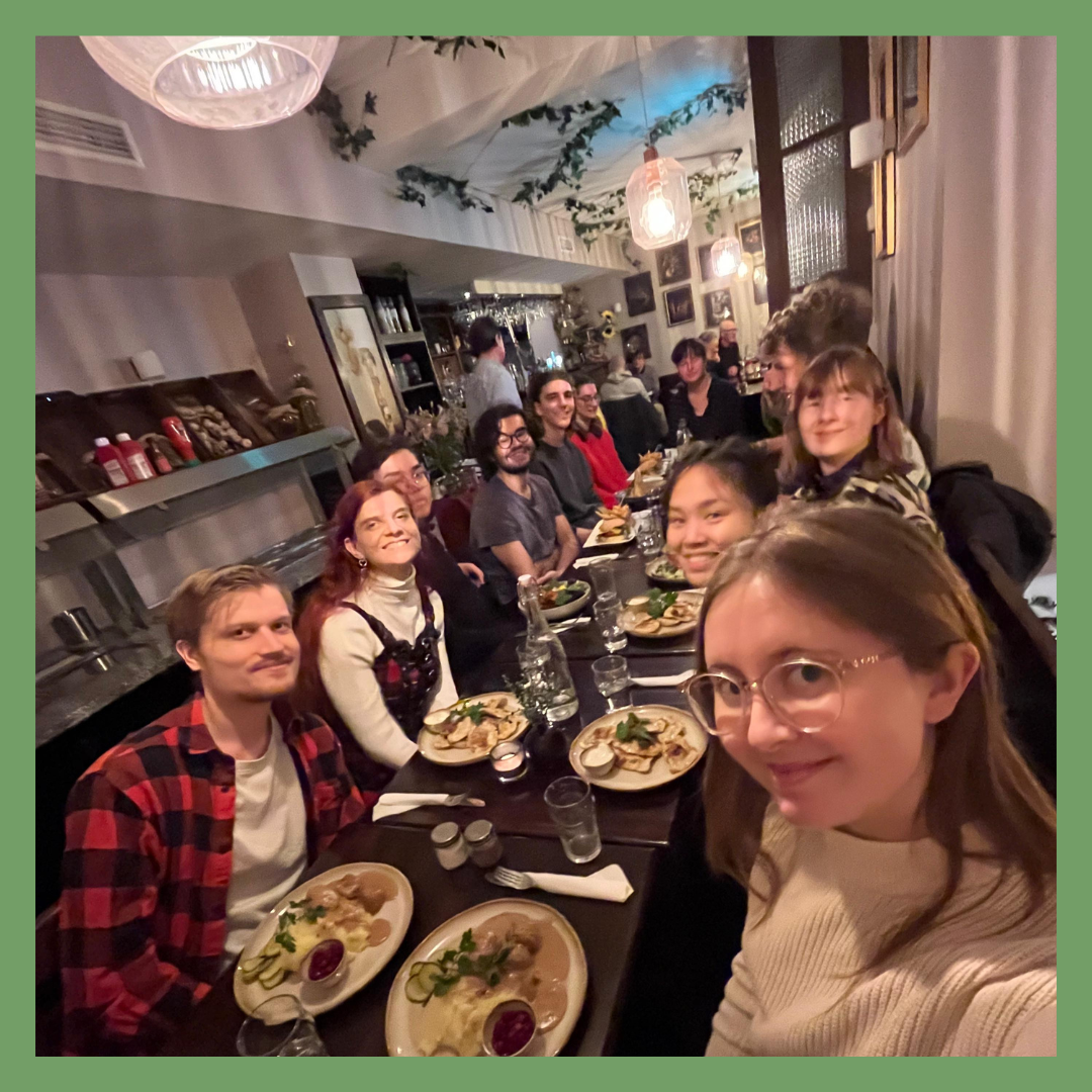 A group of people sitting at a long dining table in a restaurant, enjoying a meal together.