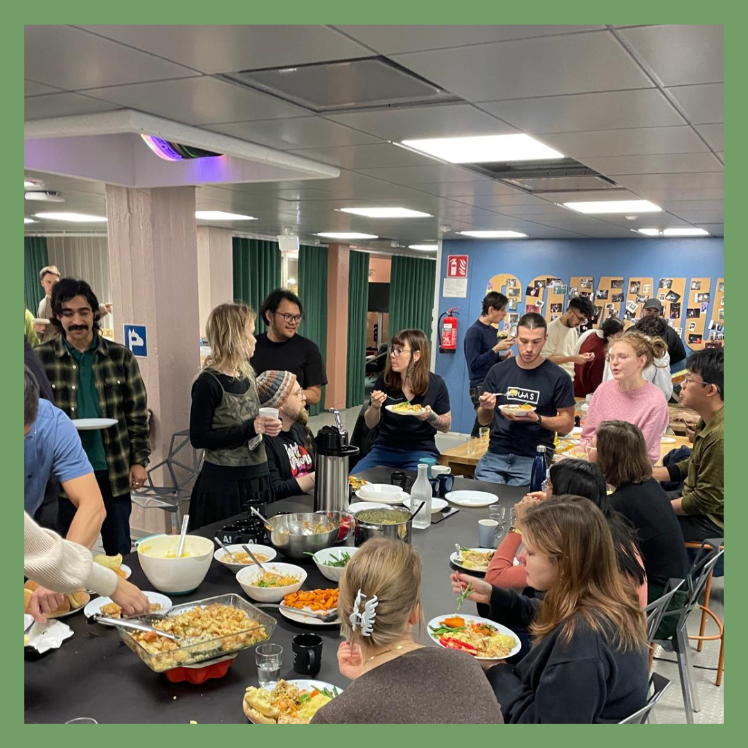 Group of people in a room enjoying a buffet-style meal with various dishes and salads on a table.