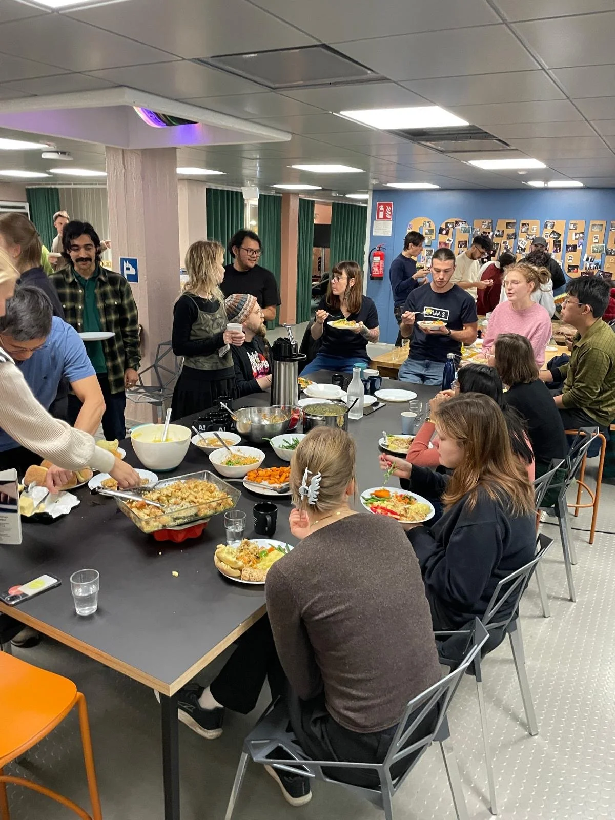 People gathered around a table enjoying a meal at a social event or celebration, with various dishes and bowls on the table.