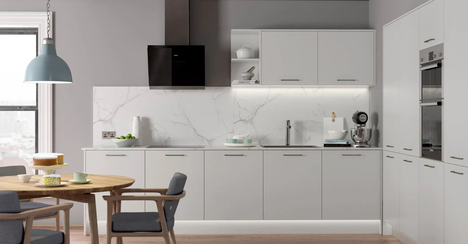 Modern white kitchen with marble backsplash, farmhouse dining table, and gray chairs, illuminated by natural light from a window.