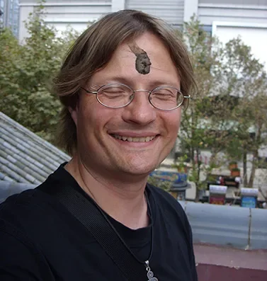 Jan Fries sonriendo con una roca en la frente, al aire libre en un entorno urbano.