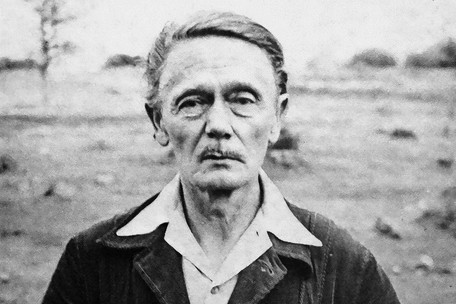 Retrato en blanco y negro de Clark Ashton Smith con cabello gris, cejas gruesas y expresión seria, vestido con una chaqueta y camisa blanca, en un entorno exterior.