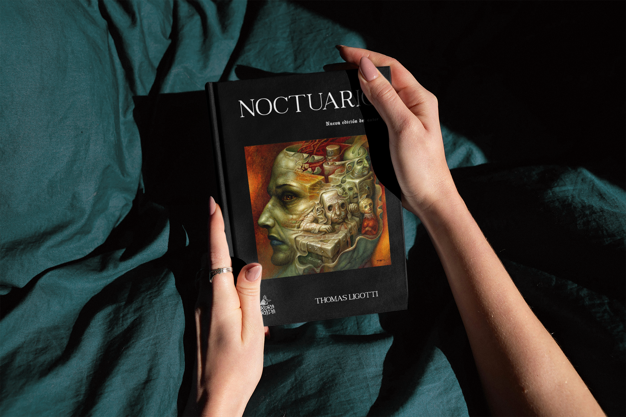 Manos sosteniendo un libro titulado 'Noctuario' con una ilustración artística en la portada que muestra un perfil humano con elementos surrealistas y rojos oscuros de fondo.